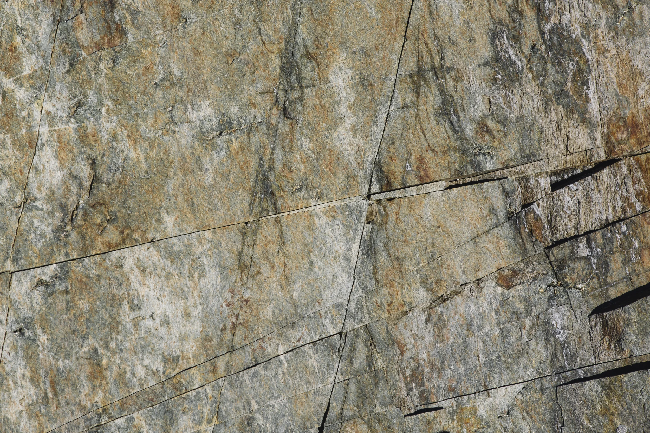 Close-up of a weathered, cracked stone wall with various shades of gray, brown, and orange.