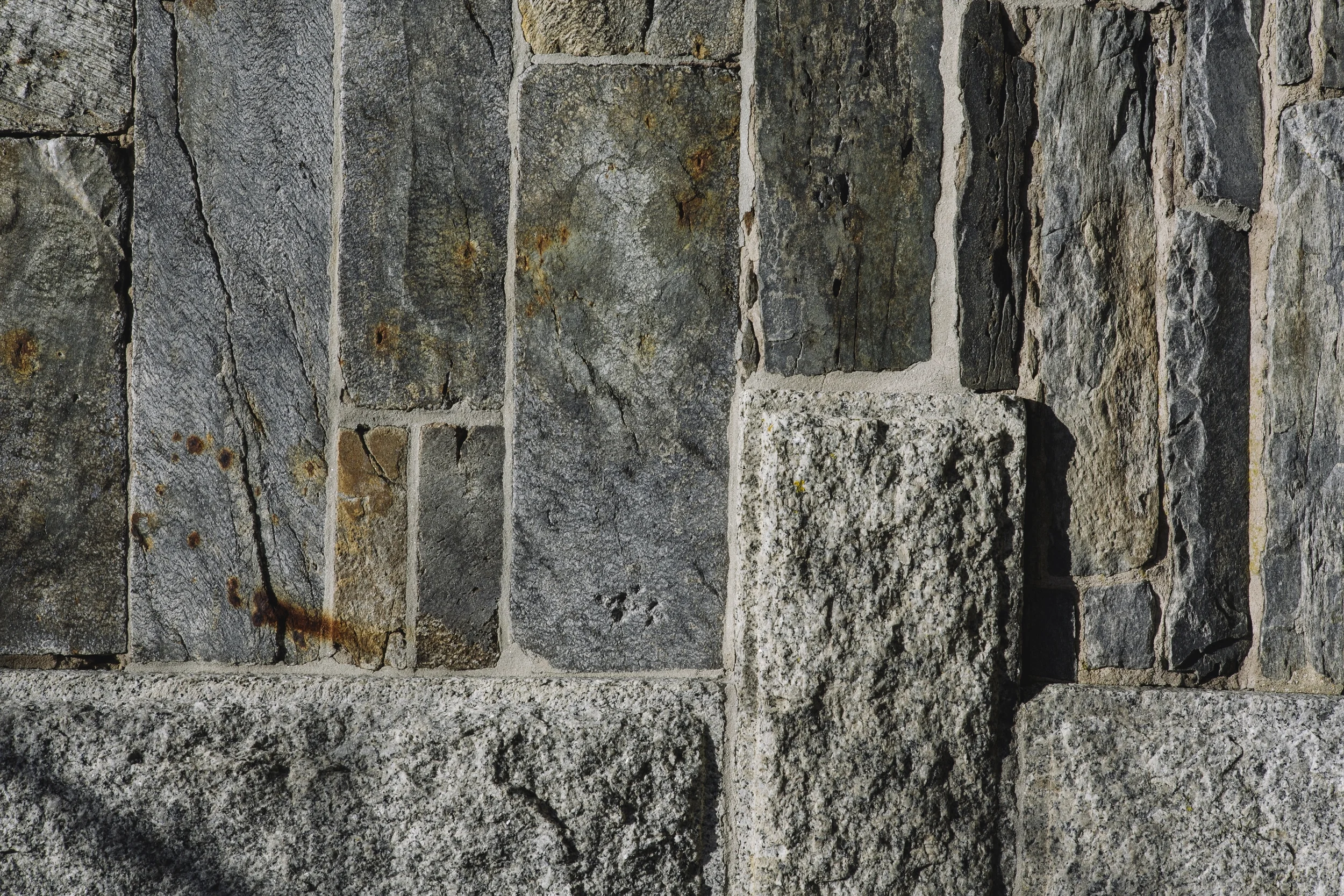 Close-up of a stone wall with irregular gray and black stones and mortar.