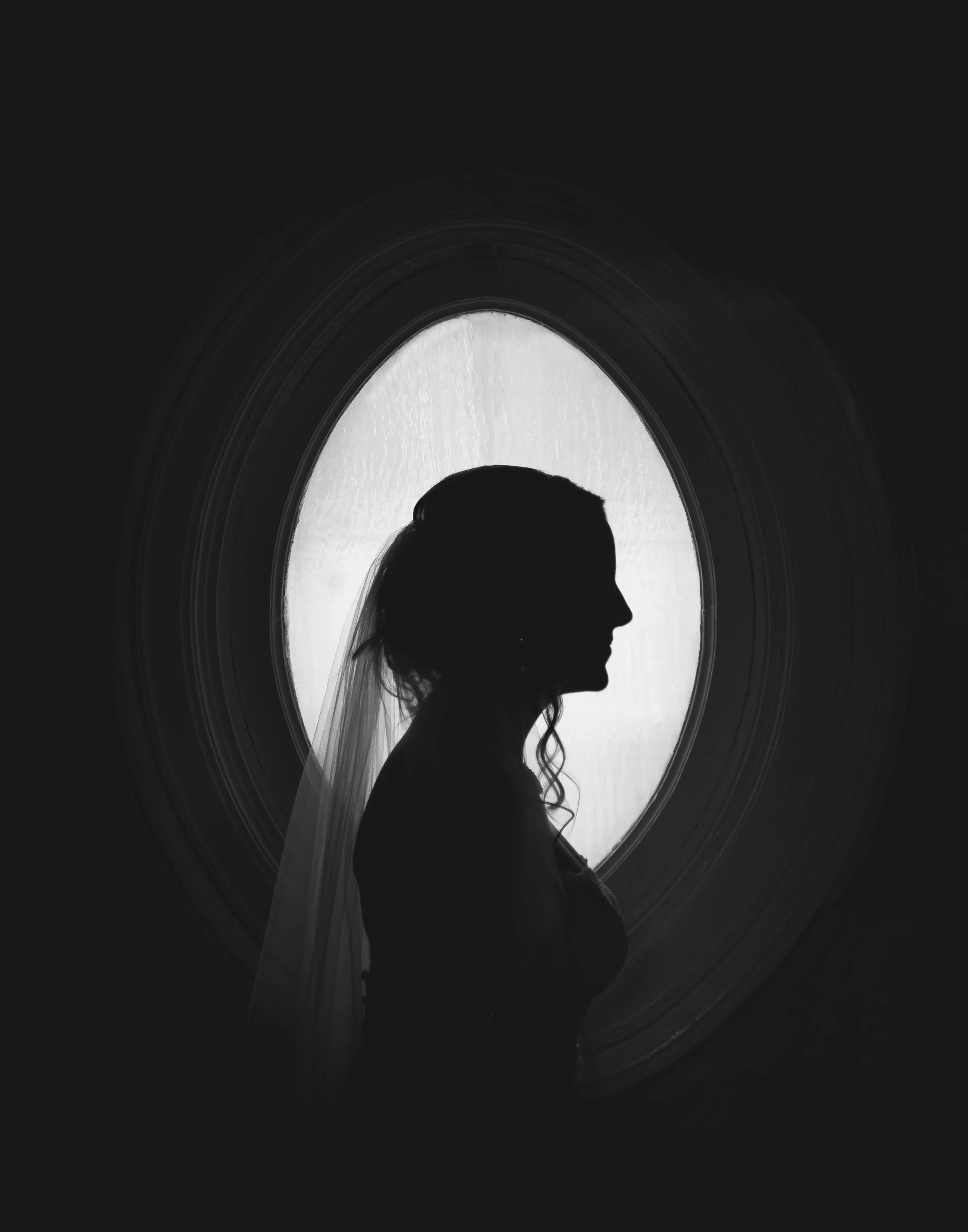 Silhouette of a woman with a veil in front of an oval window with frosted glass hayden budd photo + film new england film photographer