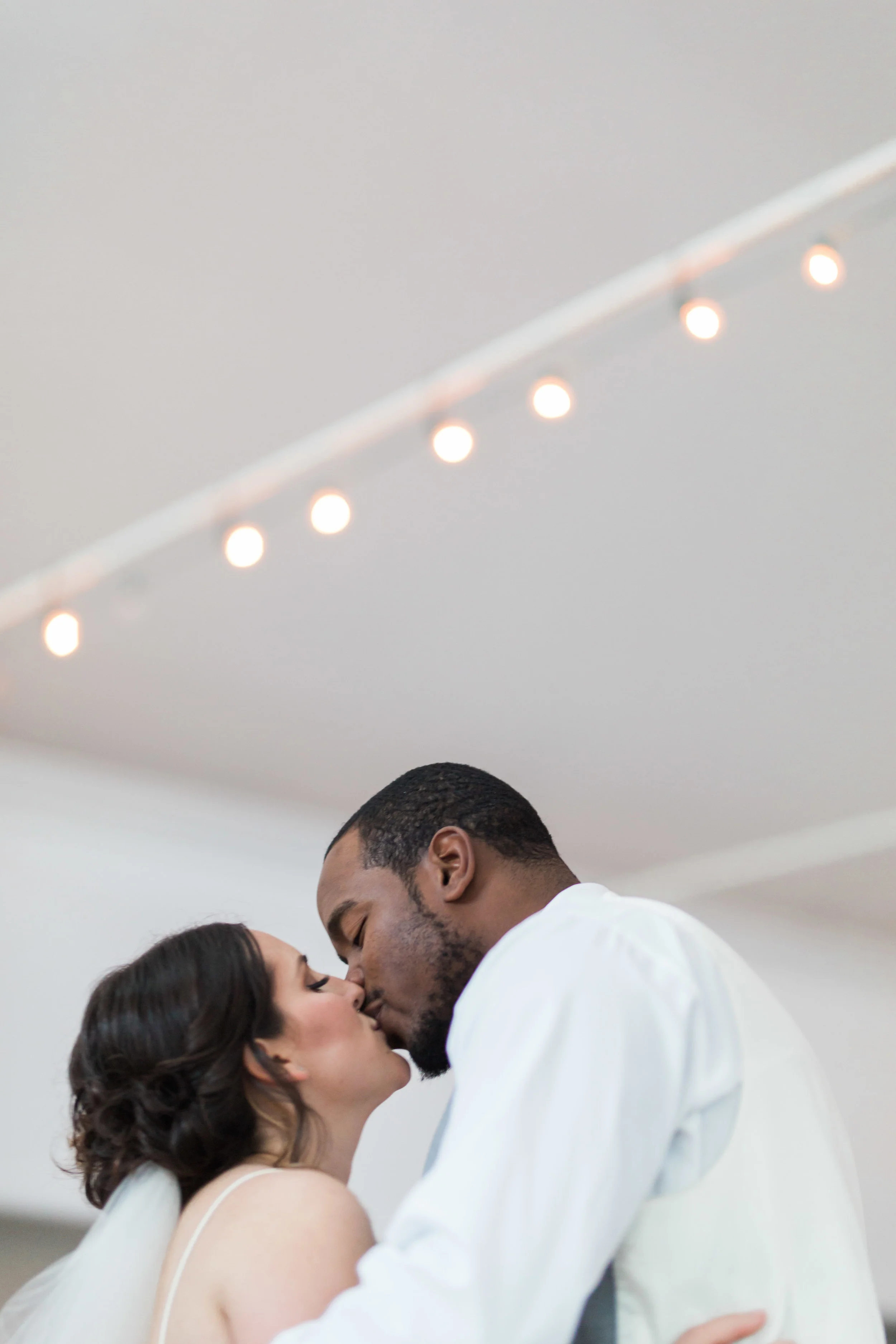A couple sharing a kiss indoors, with string lights overhead. hayden budd photo + film new england film photographer