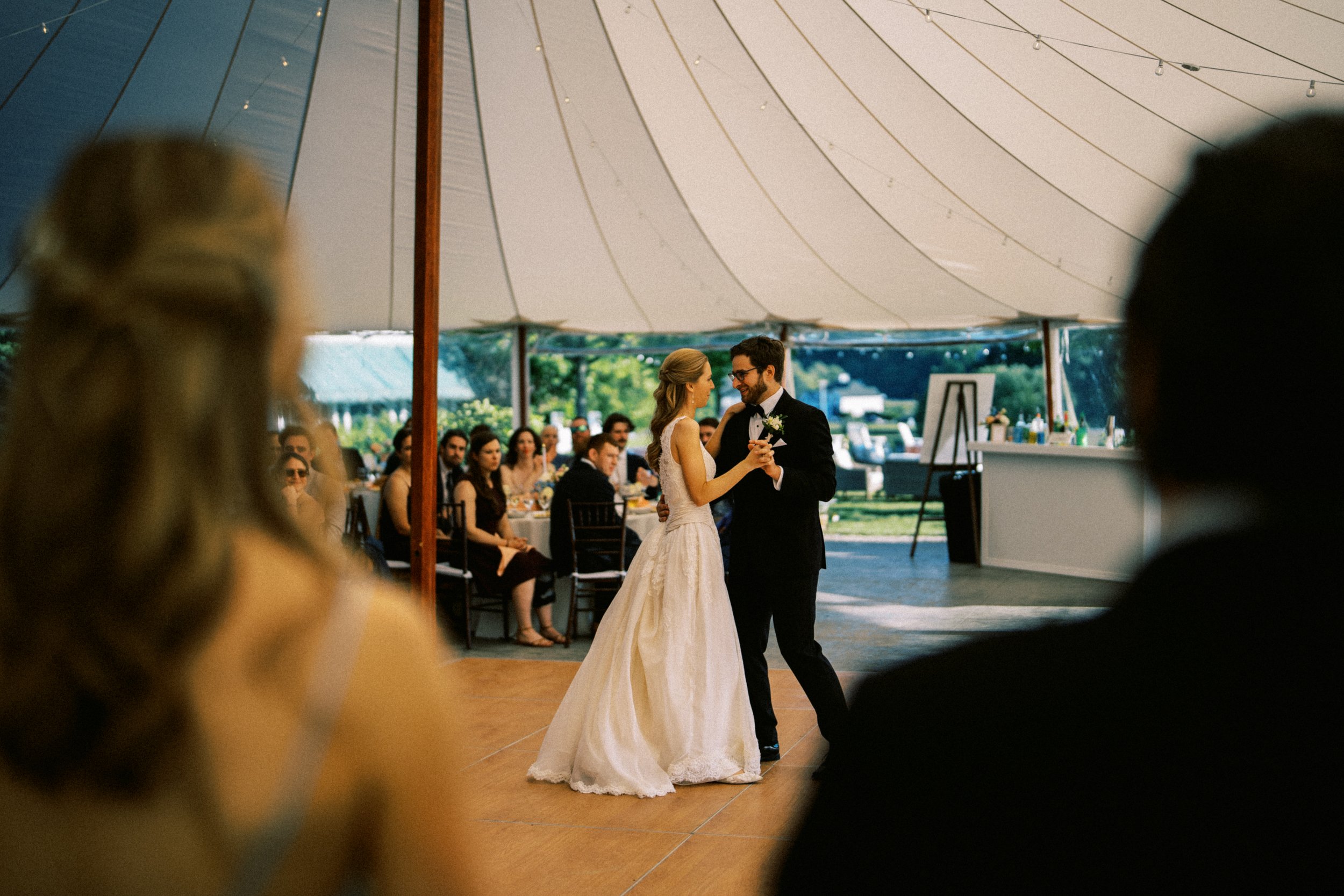 A bride and groom dancing at their wedding reception under a large tent with seated guests watching. hayden budd photo + film new england film photographer