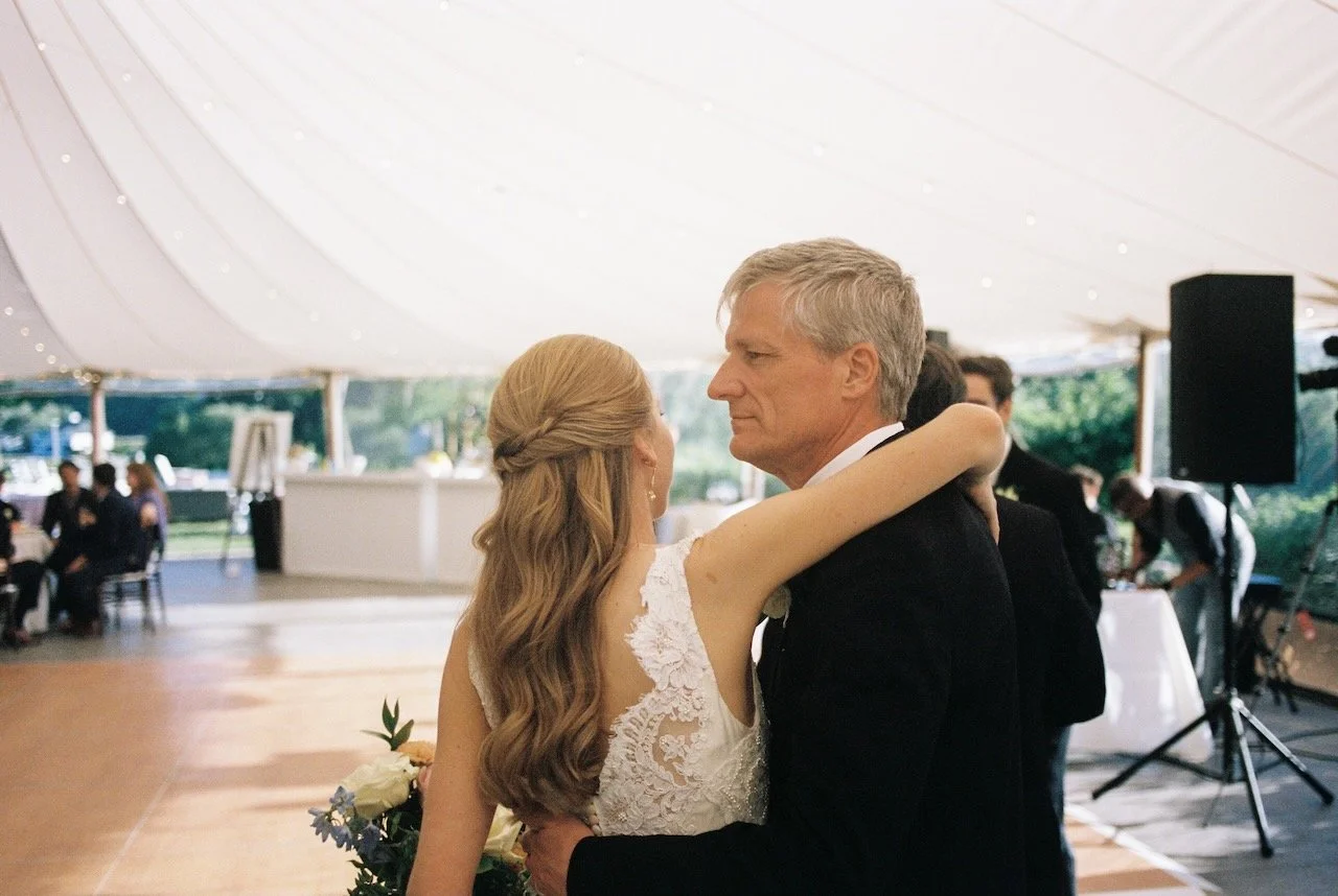 A bride and groom sharing a dance at their wedding reception, indoors under a large white tent, with guests seated in the background. hayden budd photo + film new england film photographer