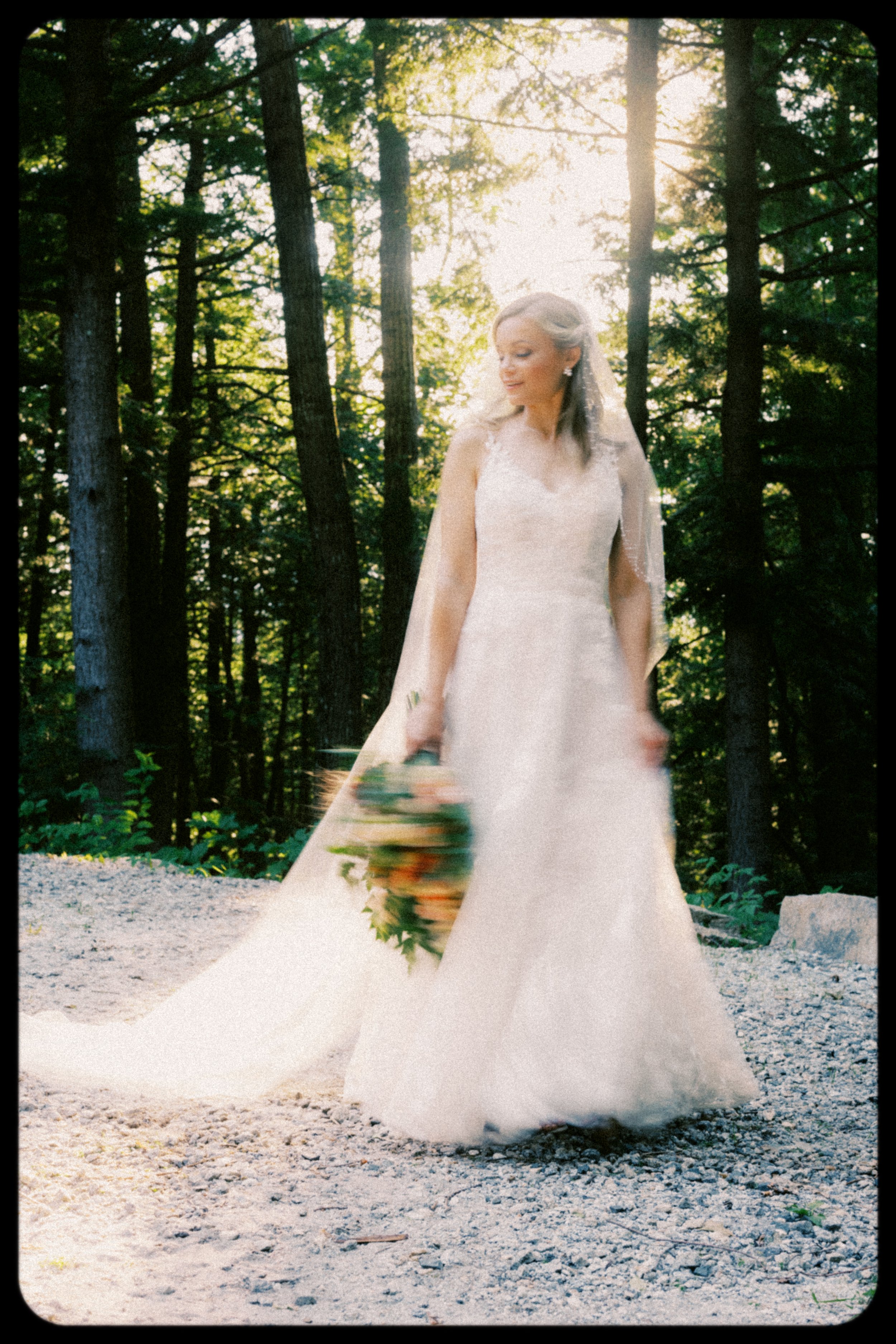 A bride in a white wedding dress holding a bouquet in a forest setting during sunset.