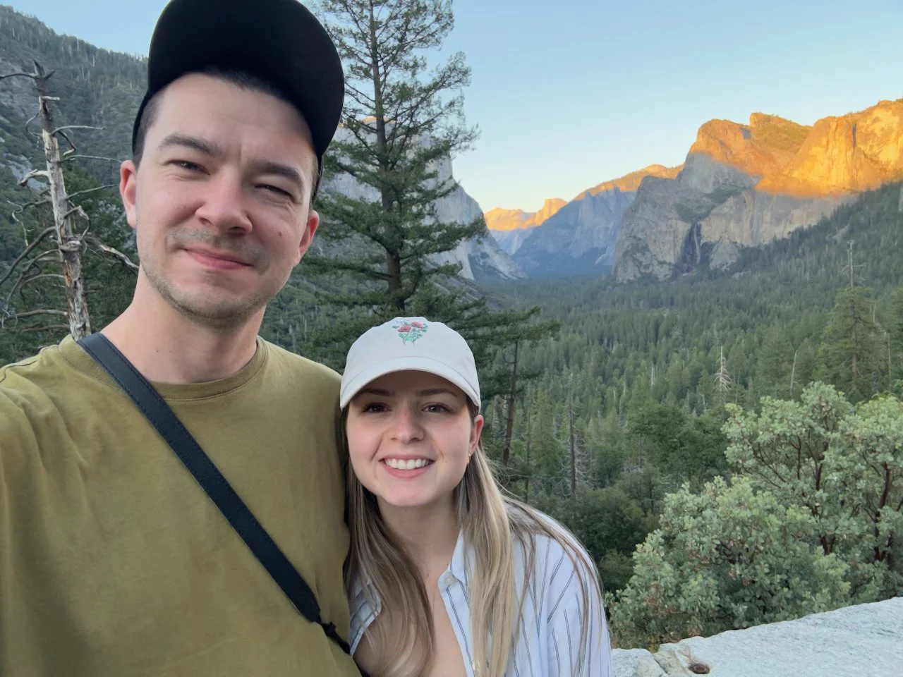 hayden budd photo + film new england film photographer A smiling man and woman taking a selfie against a mountainous forest landscape at sunset.