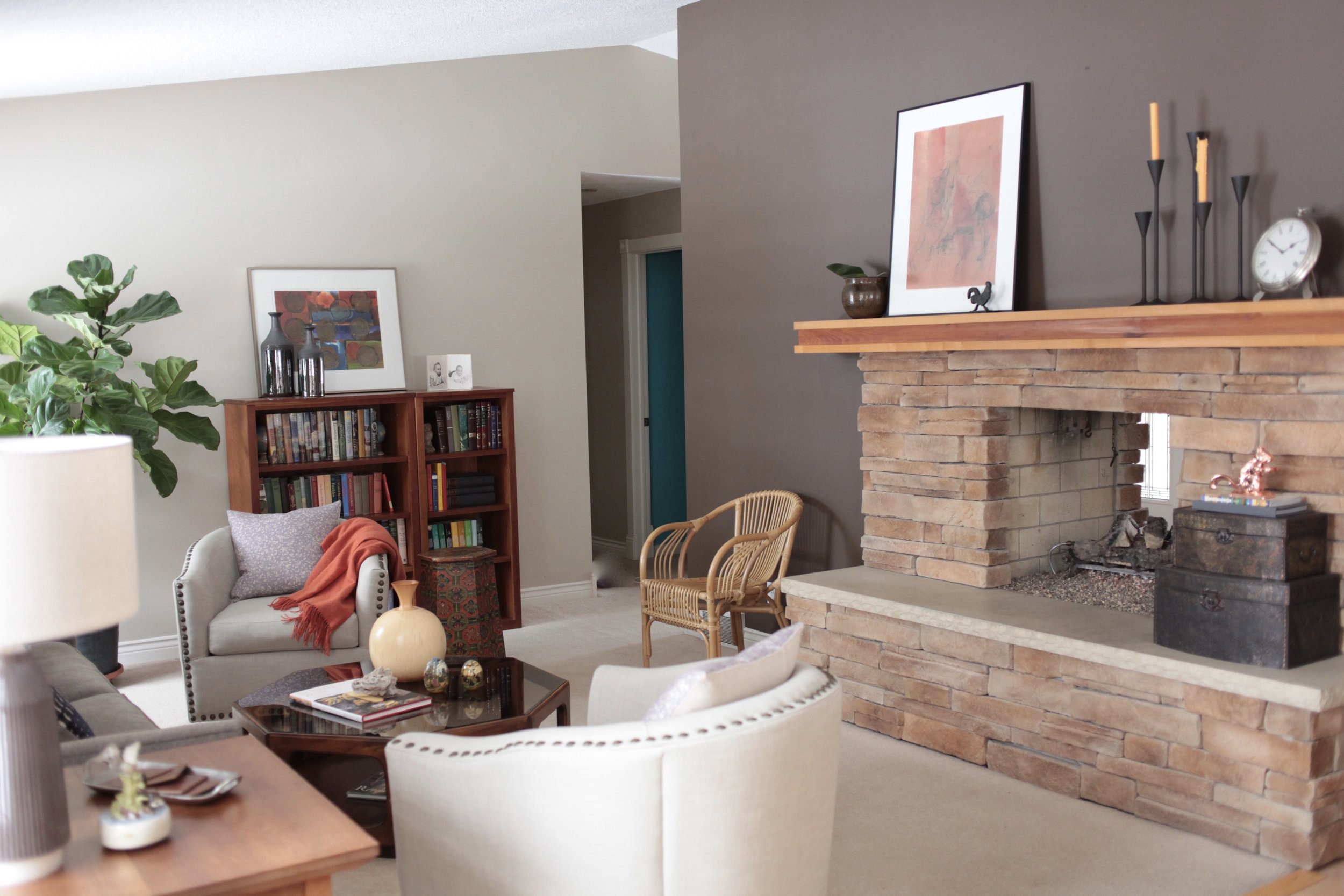 A neutral space with large fireplace, pops of orange, fig tree, and wicker chair.jpeg