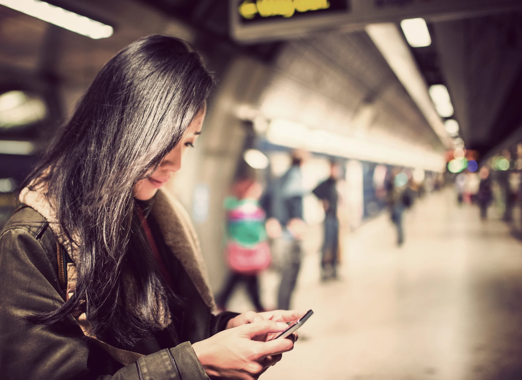 Kvinna som väntar på tunnelbana och läser på sin telefon
