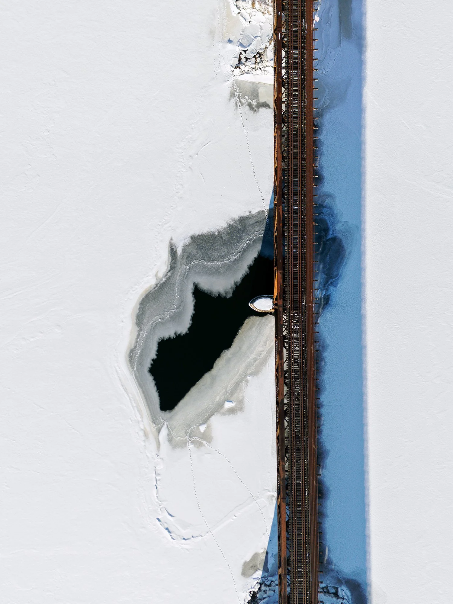 An image of a train bridge across a frozen river, taken from a drone