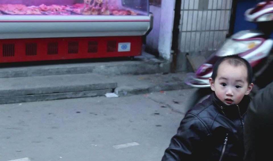   Zhongzhou, China  / Feb 5, 2012     A young boy catches glimpse of the camera as he makes his way down a street market.&nbsp; 