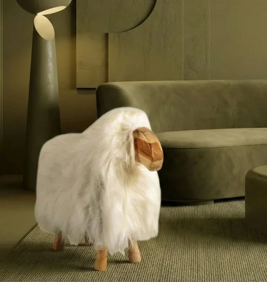 A plush sheep with wooden legs and a wooden face standing by a green upholstered couch in a modern living room.
