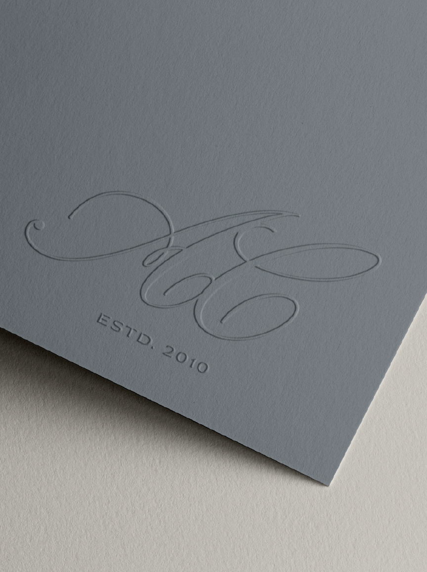 Close-up of a light gray paper with embossed elegant cursive initials 'E' and 'L', and the text 'ESTD. 2010' below.