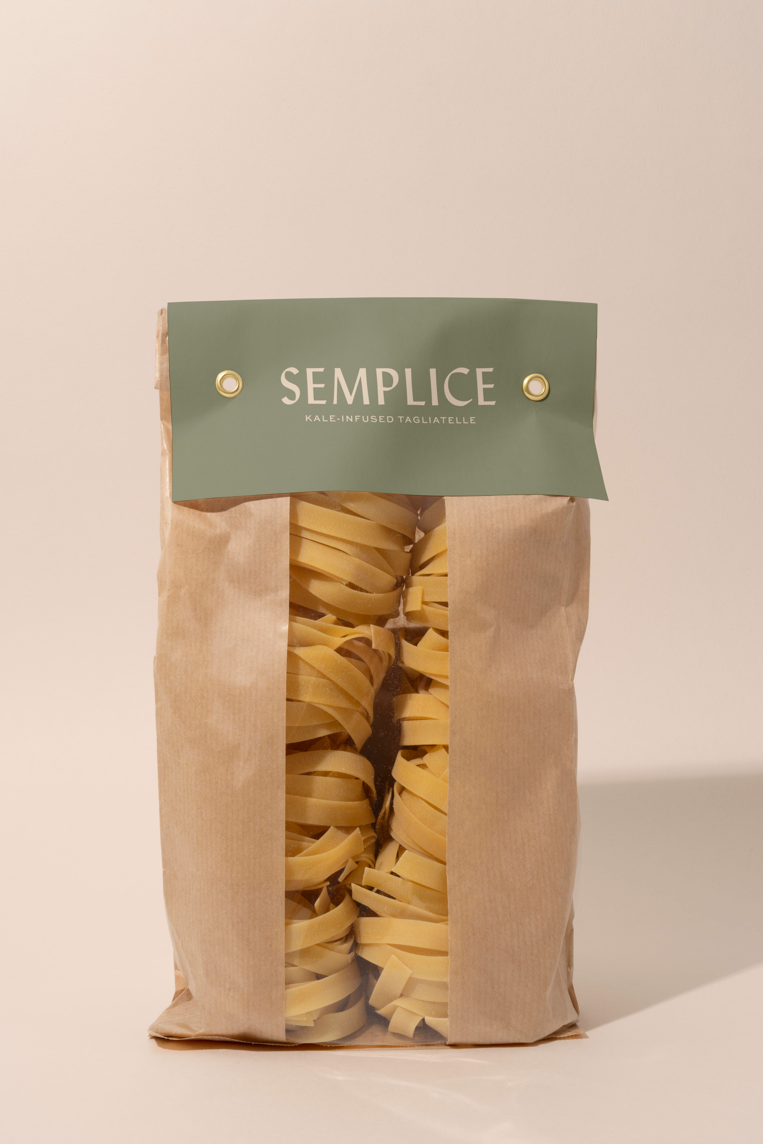 Package of Semplice kale-infused tagliatelle pasta with a green label on a brown paper bag, partially see-through showing the pasta inside, against a plain beige background.