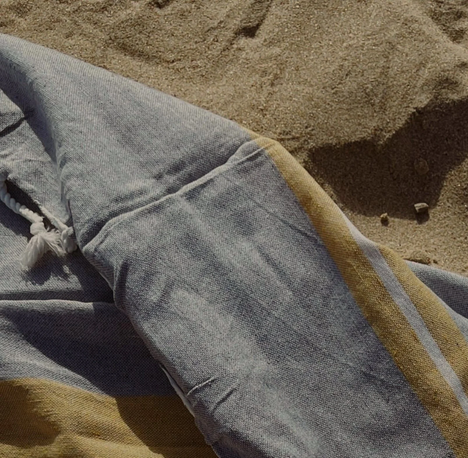 A close-up of a pair of gray jeans with white drawstrings, lying on sandy ground.