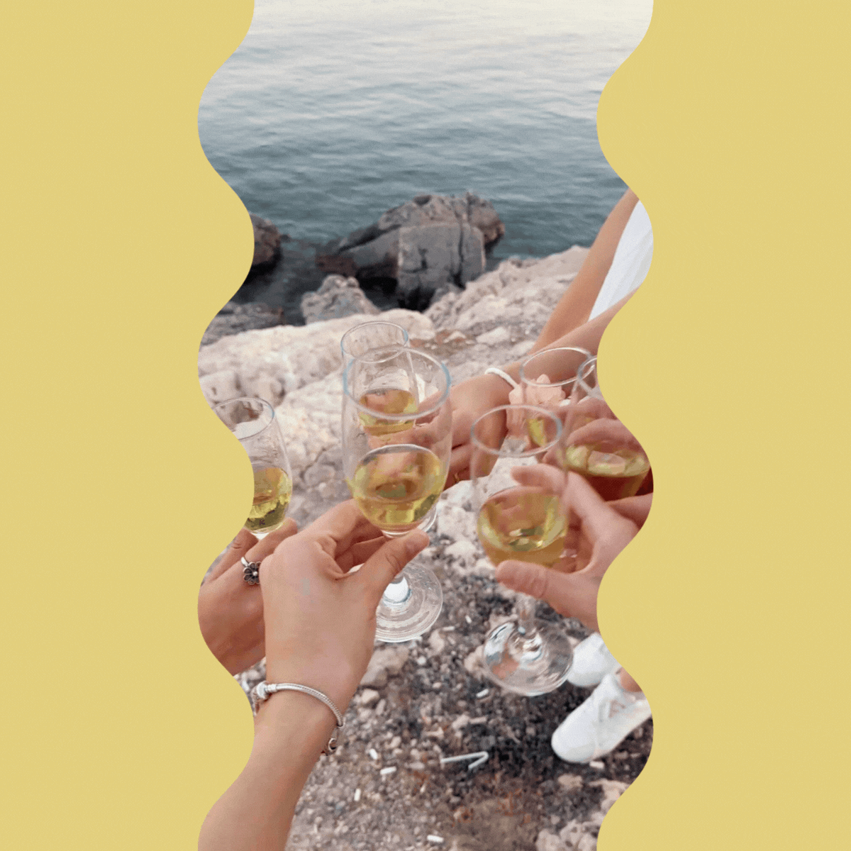 People toasting with glasses of white wine by a rocky lakeside or seaside.