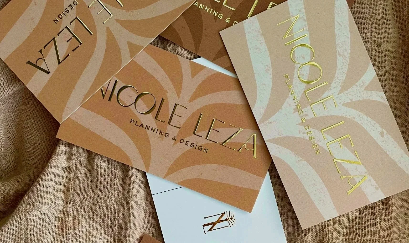 Multiple business cards for Nicole Leza Planning & Design on a beige textured fabric surface.