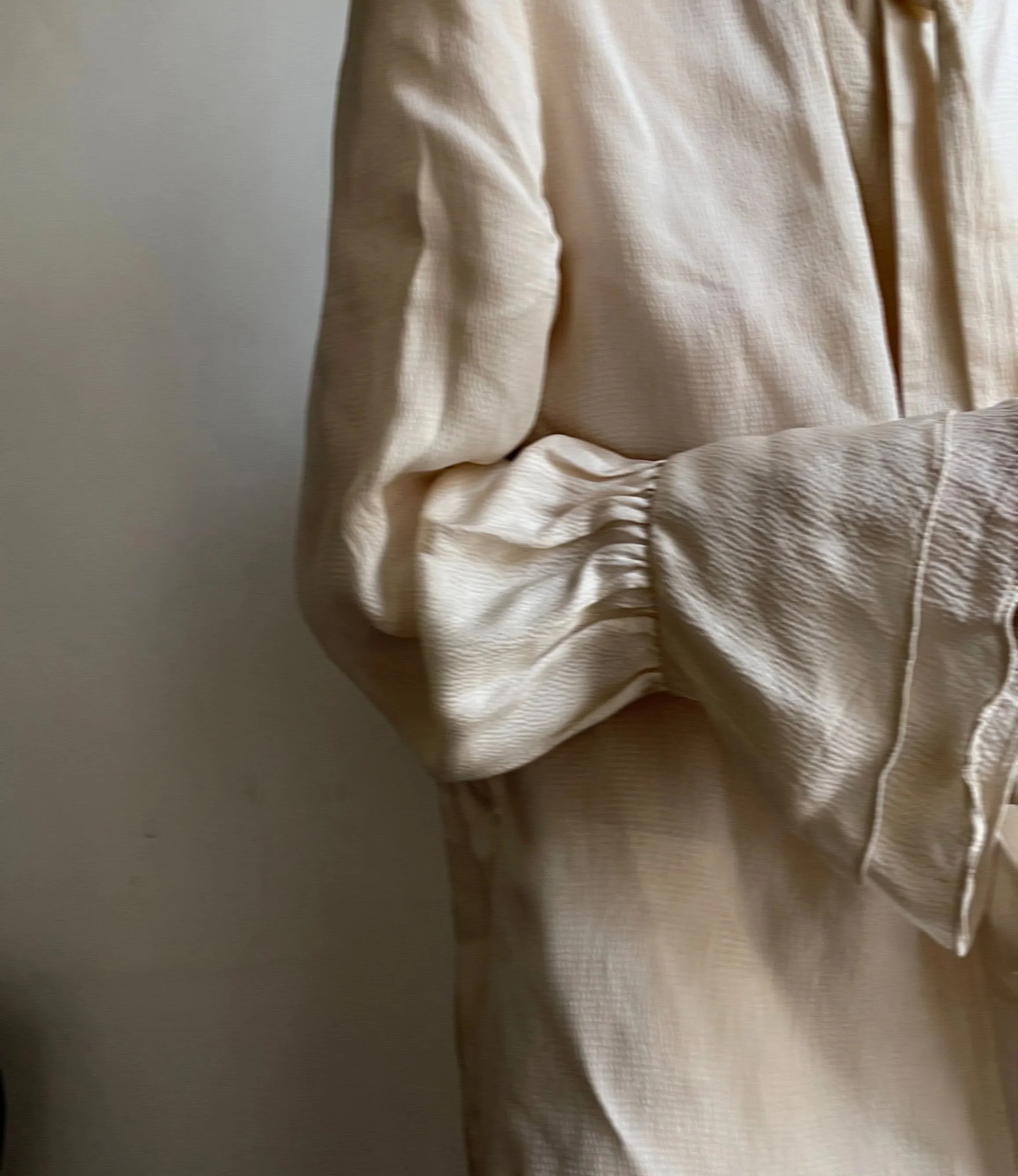 Close-up of beige, textured fabric clothing, possibly a soft jacket or coat, with ripples and folds.
