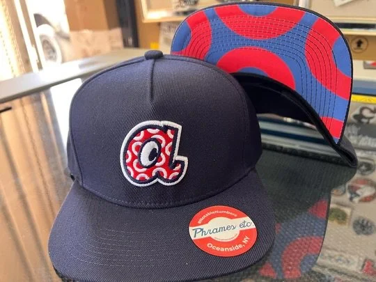 This limited edition of the Phish and Braves mashup hat features a classic navy wool blend flat bill snapback design. It is adorned with striking 3D puff embroidery and embellished with captivating donut art beneath the brim. Elevate your look with t