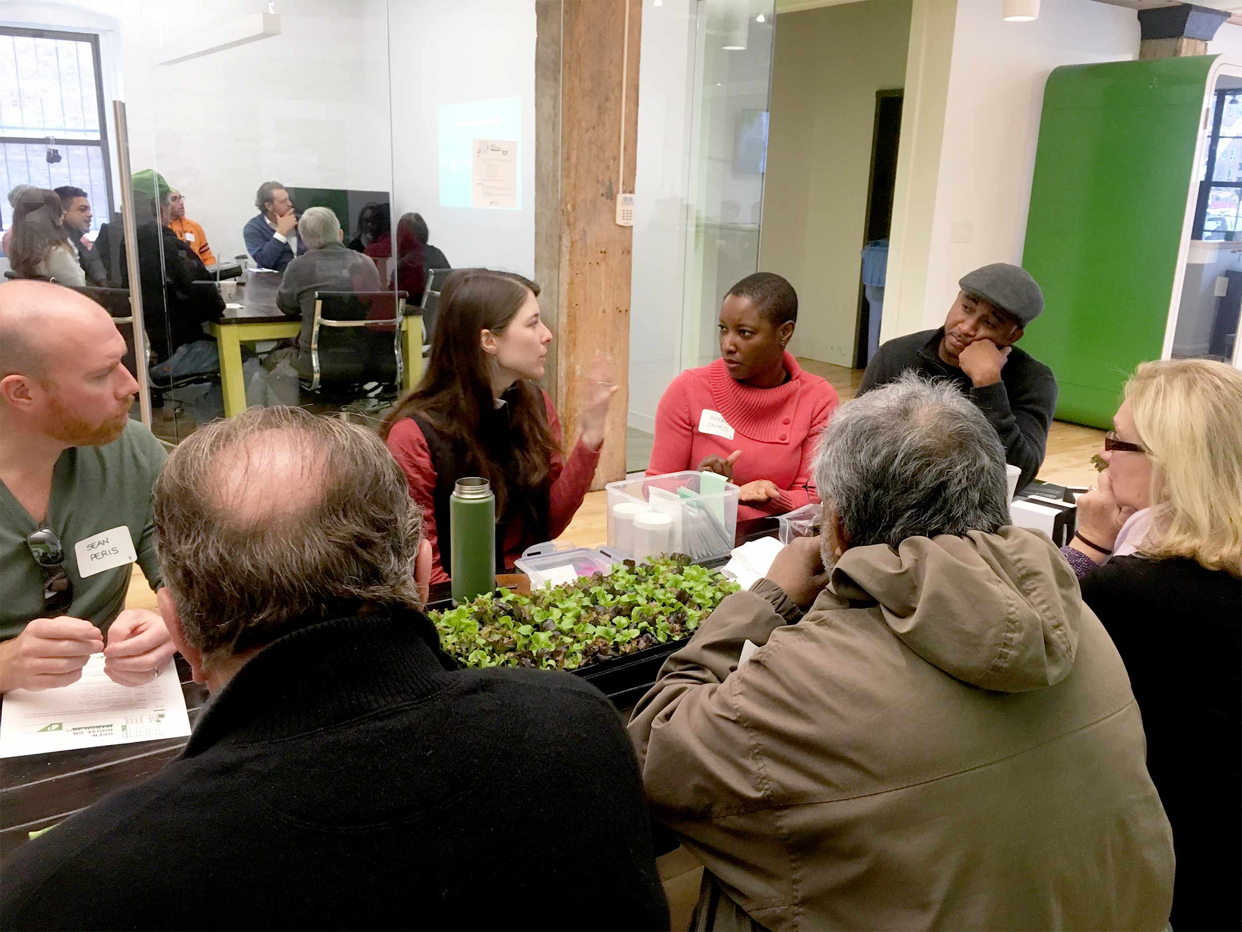 Jaime answers a question from an open house participant. She has some live seedlings on the table that were used during the session to demonstrate how to successfully transplant seedlings into the crop columns.