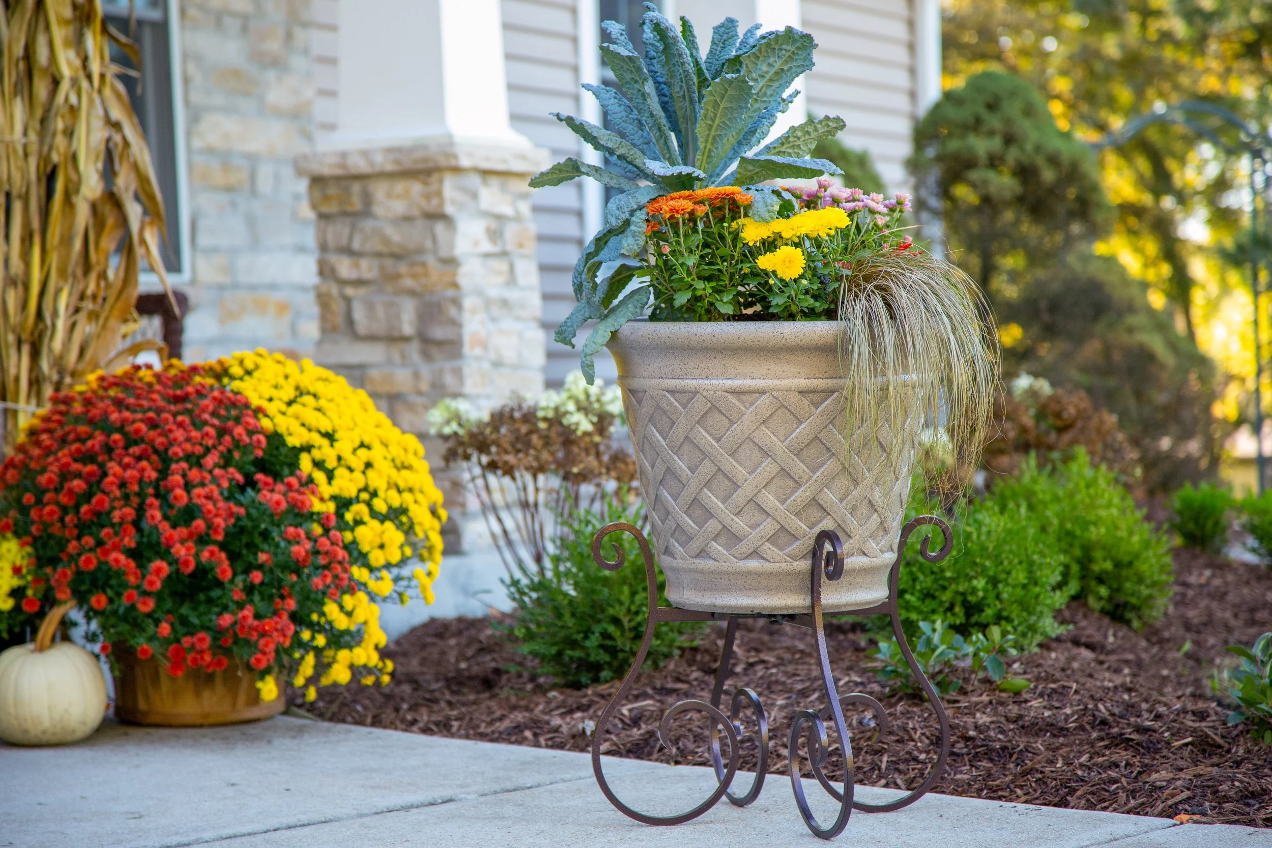 Flowers in a planter on a Gardien plant stand by a front porch