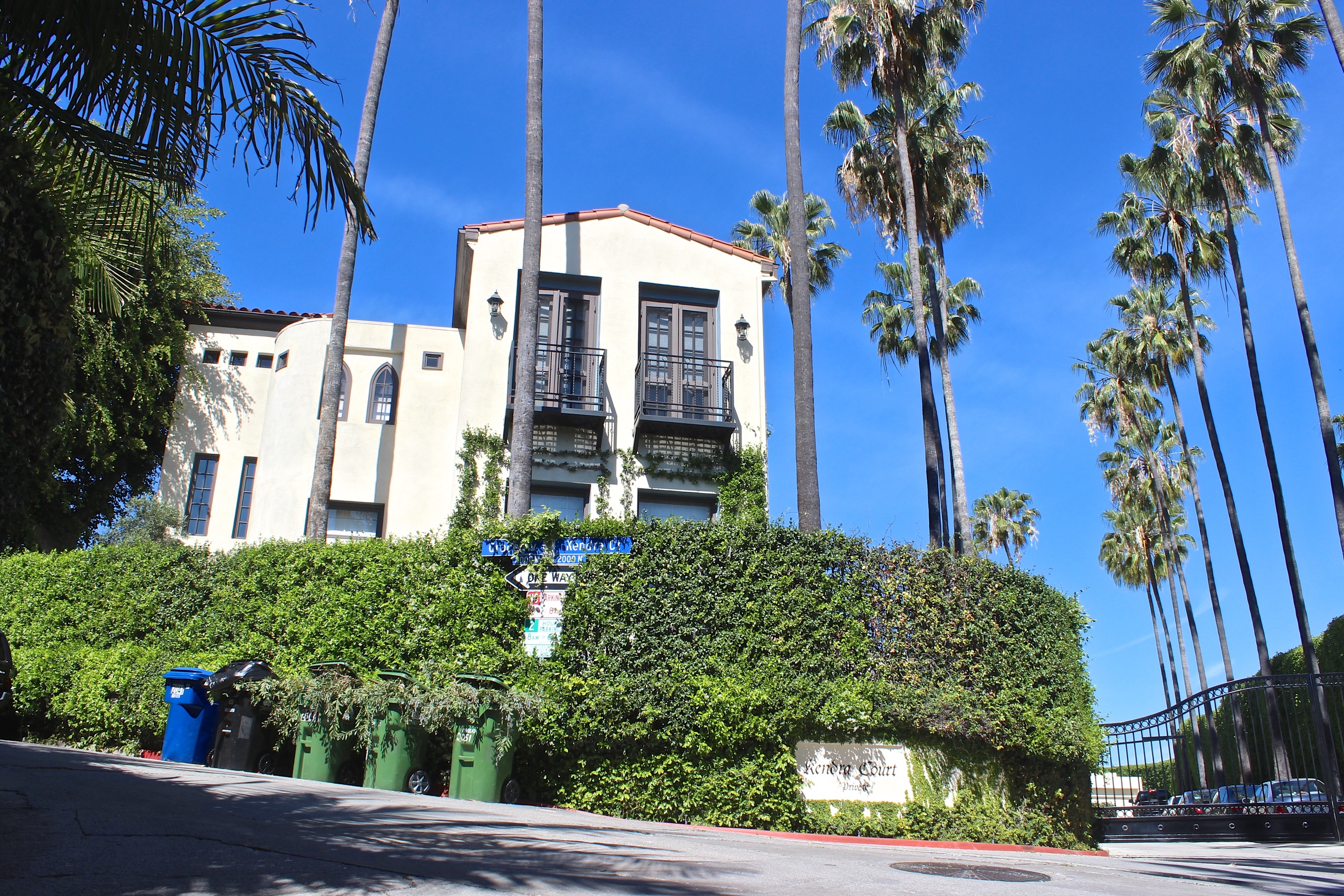 Mission style multi unit condo with a vine covered wall and palm trees lining the gated parking area.