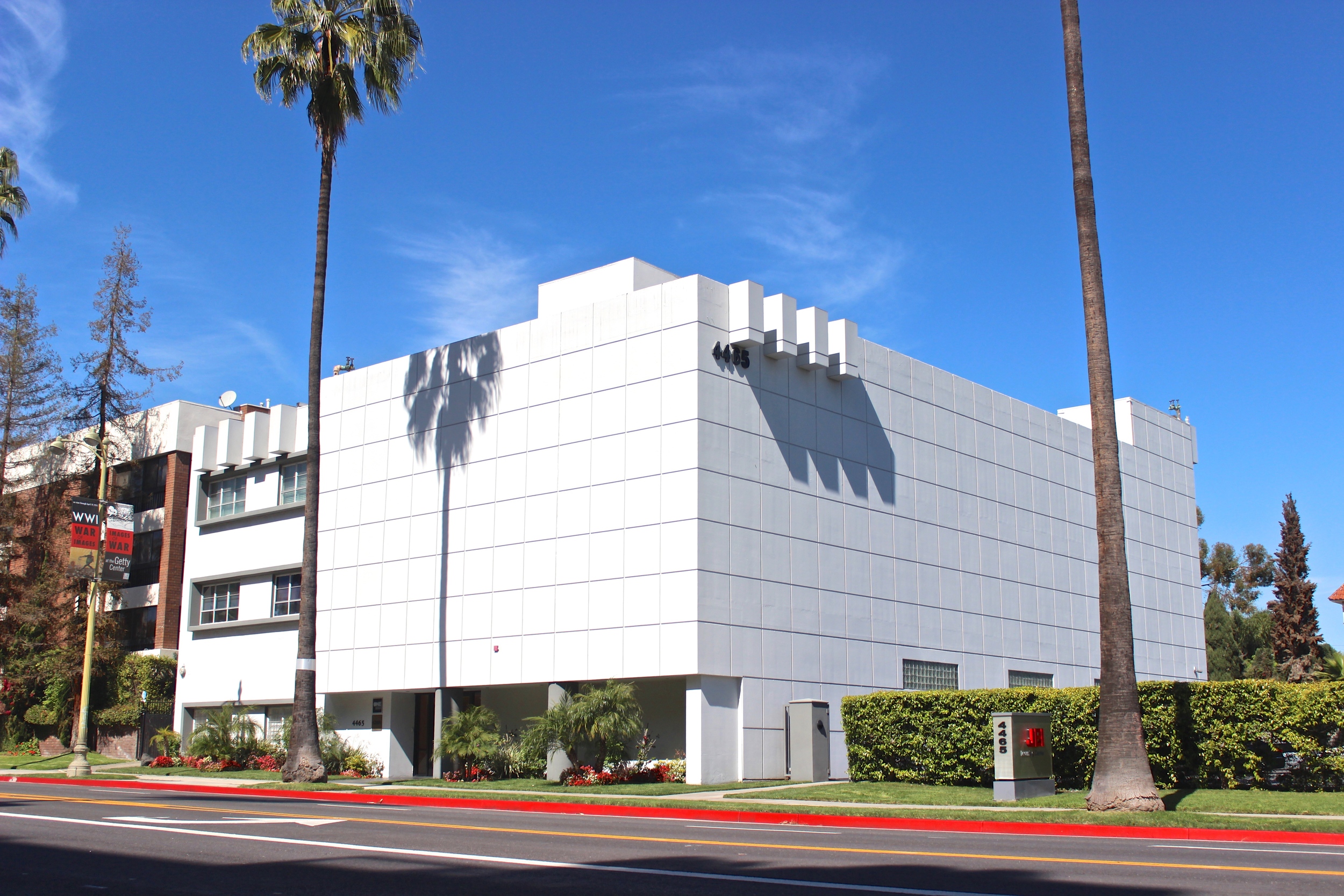 Modern white office building on a palm tree lined street.
