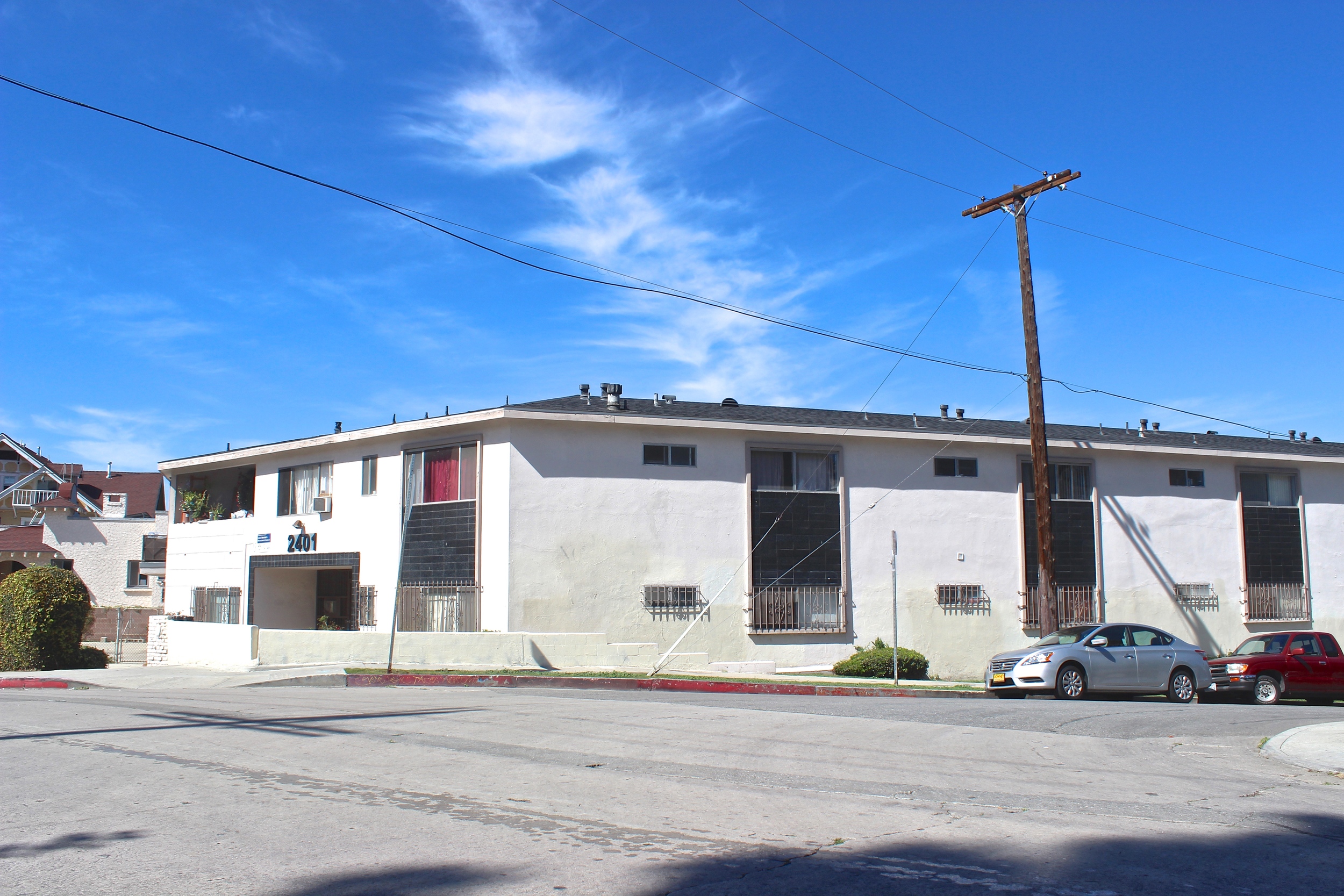 Two story white apartment building with black accents along with street parking.