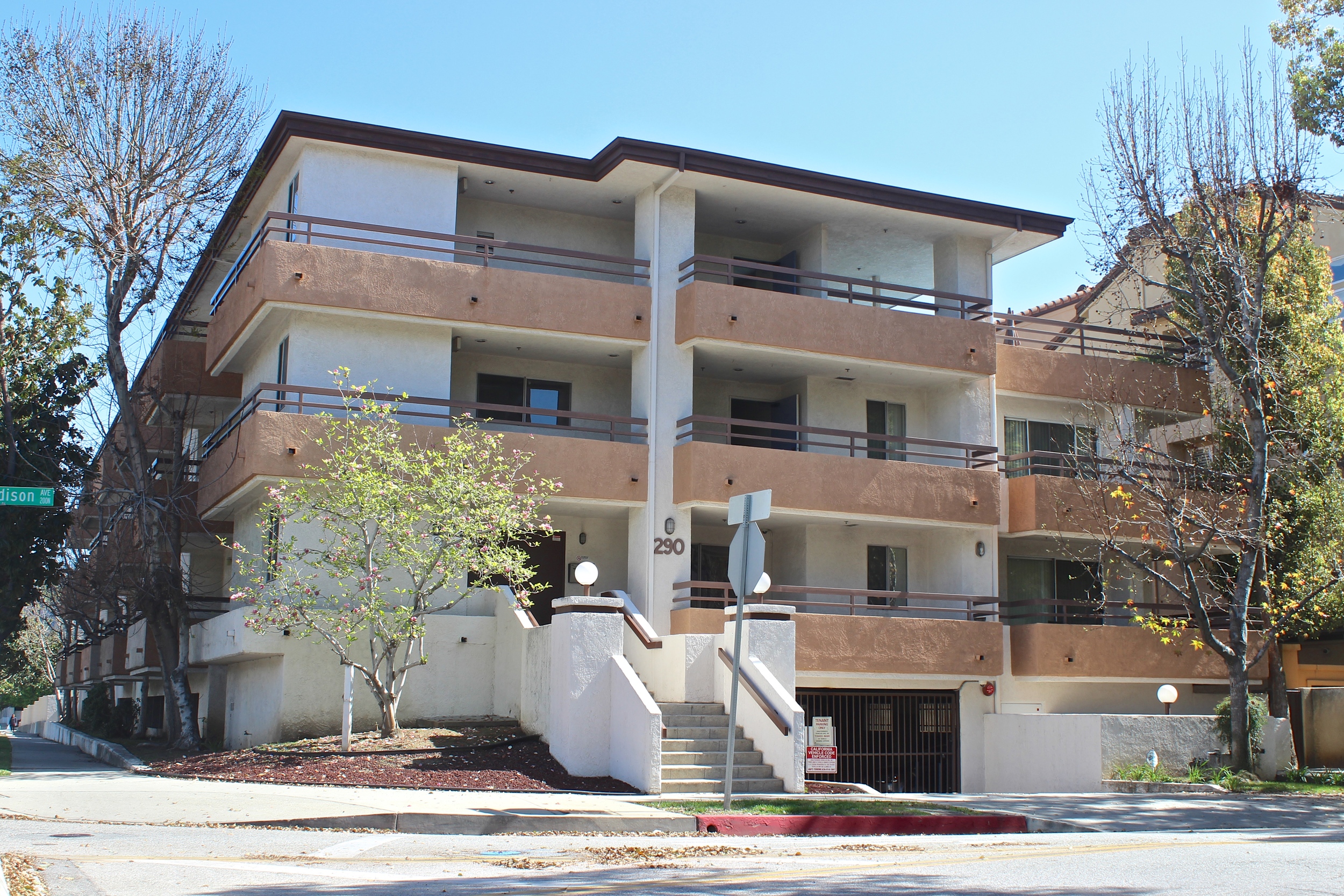 Three story white apartment building with balconies facing the street and gated subterranean garage.