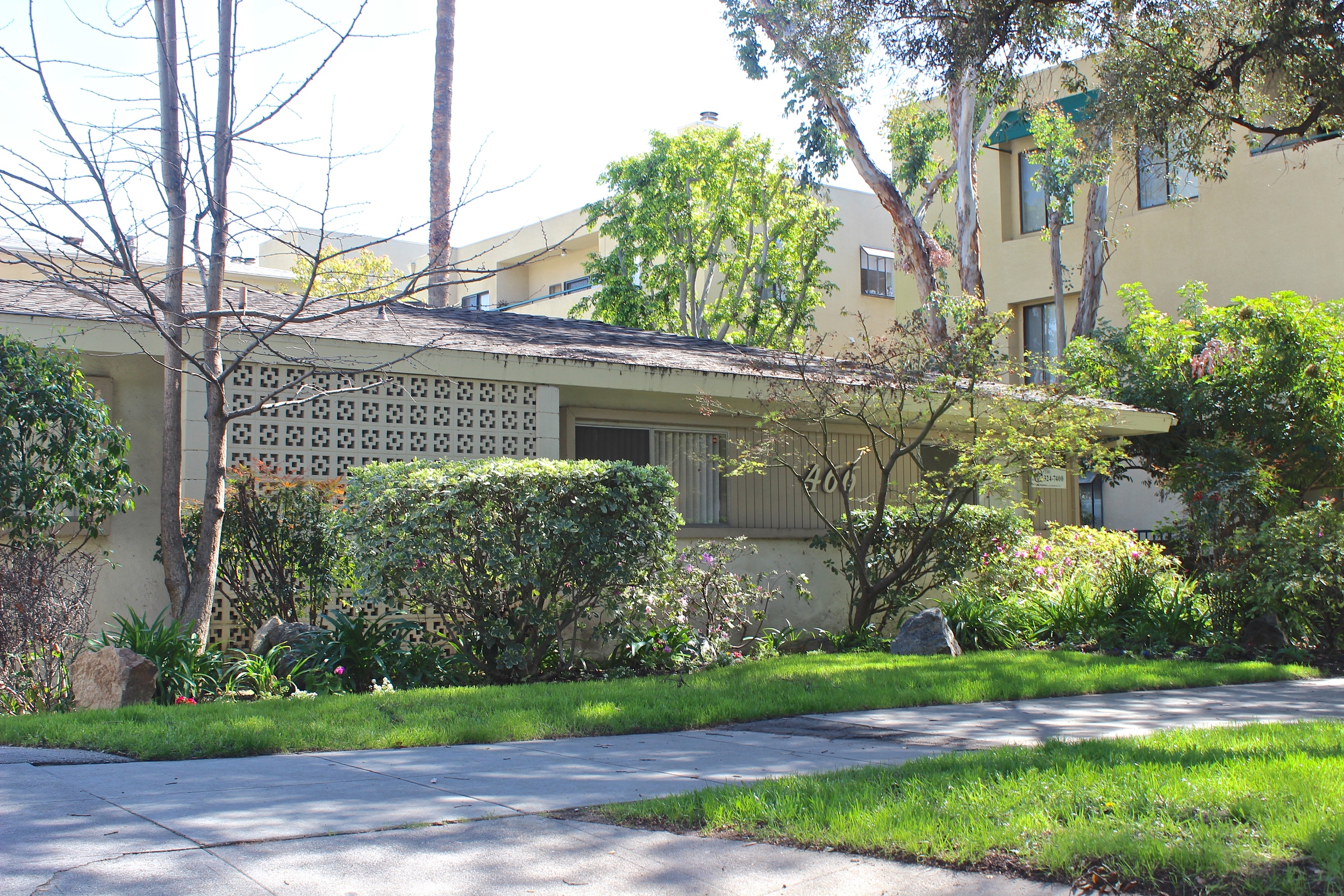 Shrubs and trees surrounding gray townhouse with gray roof.