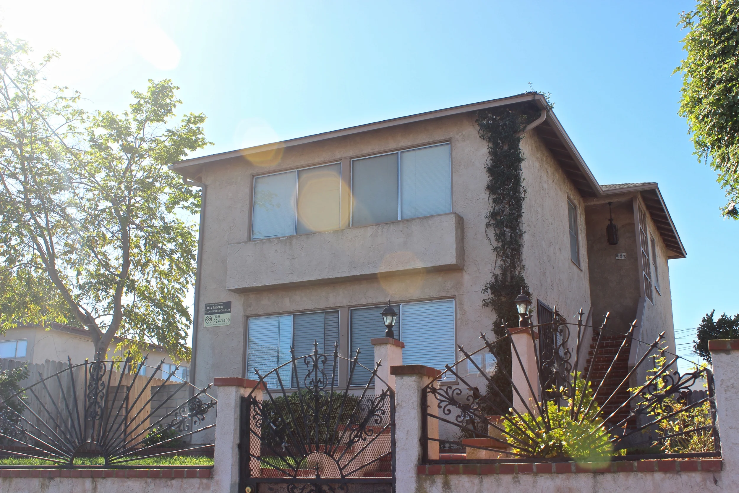 Two-story house with lens flare, ornate fence, and climbing plants.
