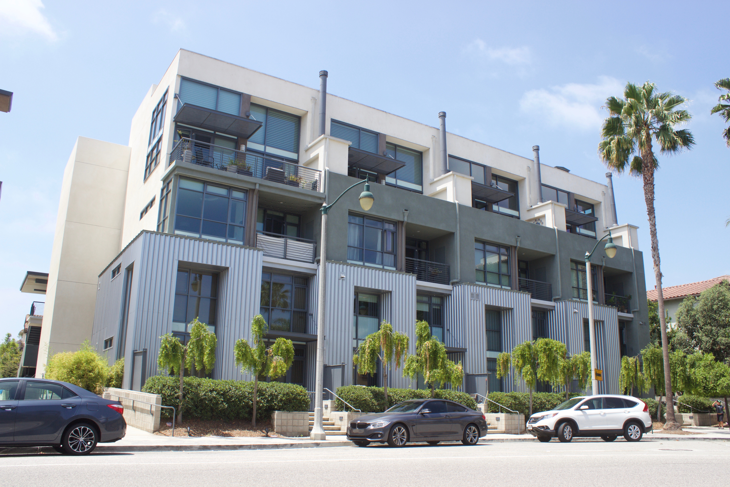 Three story modern metal, grey, and white condominium with street parking.