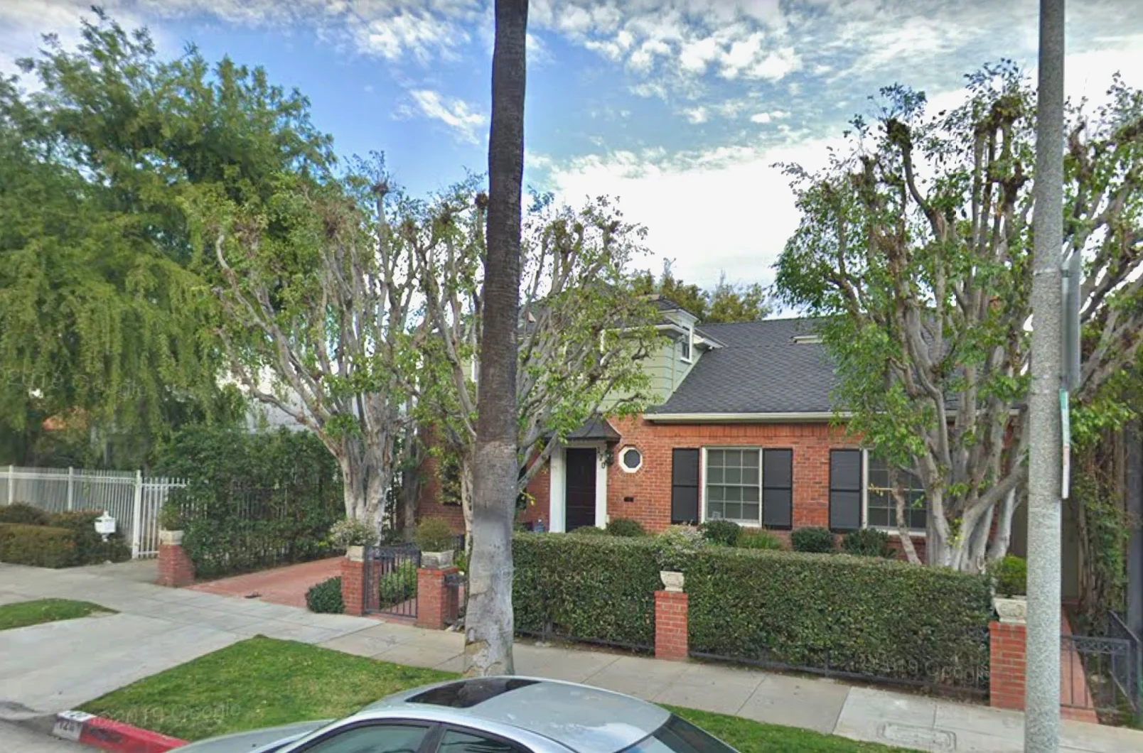 Brick single family home in neighborhood with brick driveway and a shrub wall in front yard. 