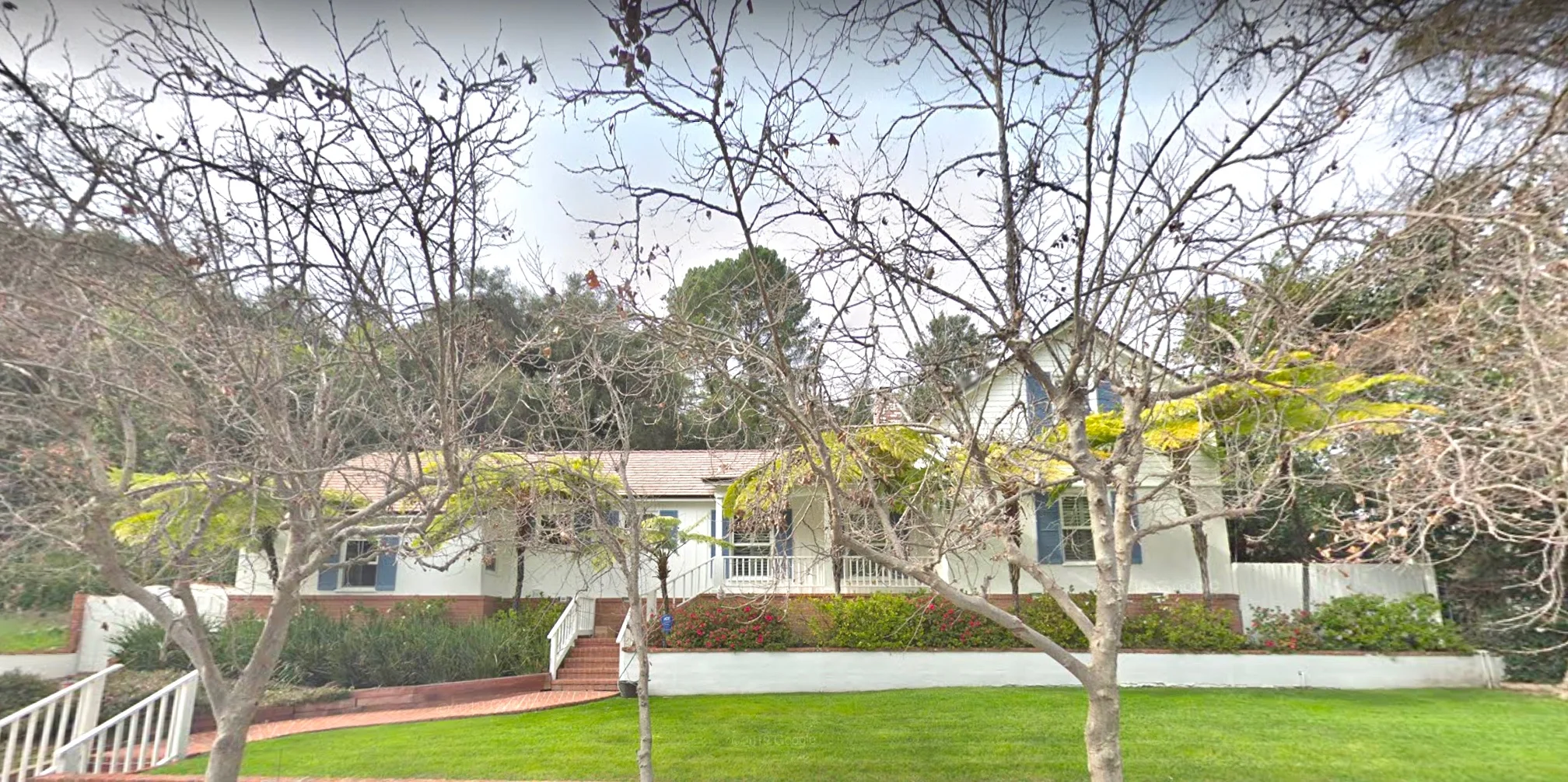 White ranch style single family home with large front lawn and red brick path.
