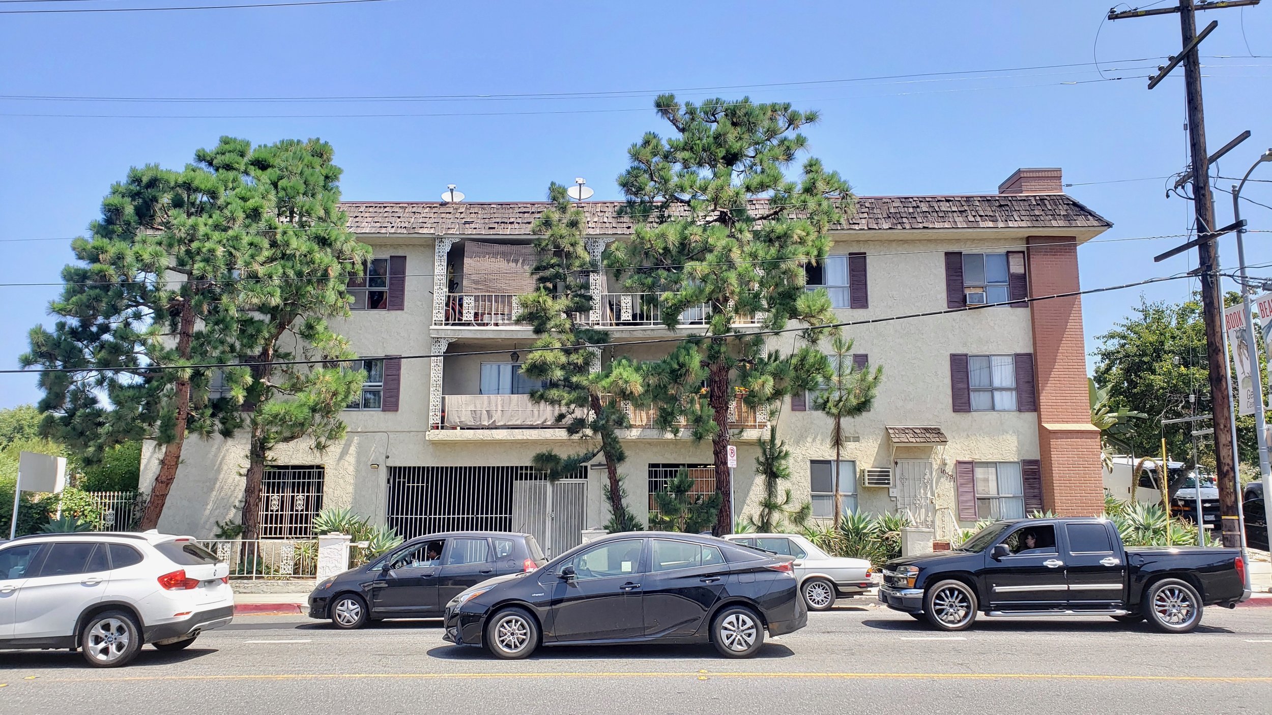 Street level view of apartment complex with large pine trees.