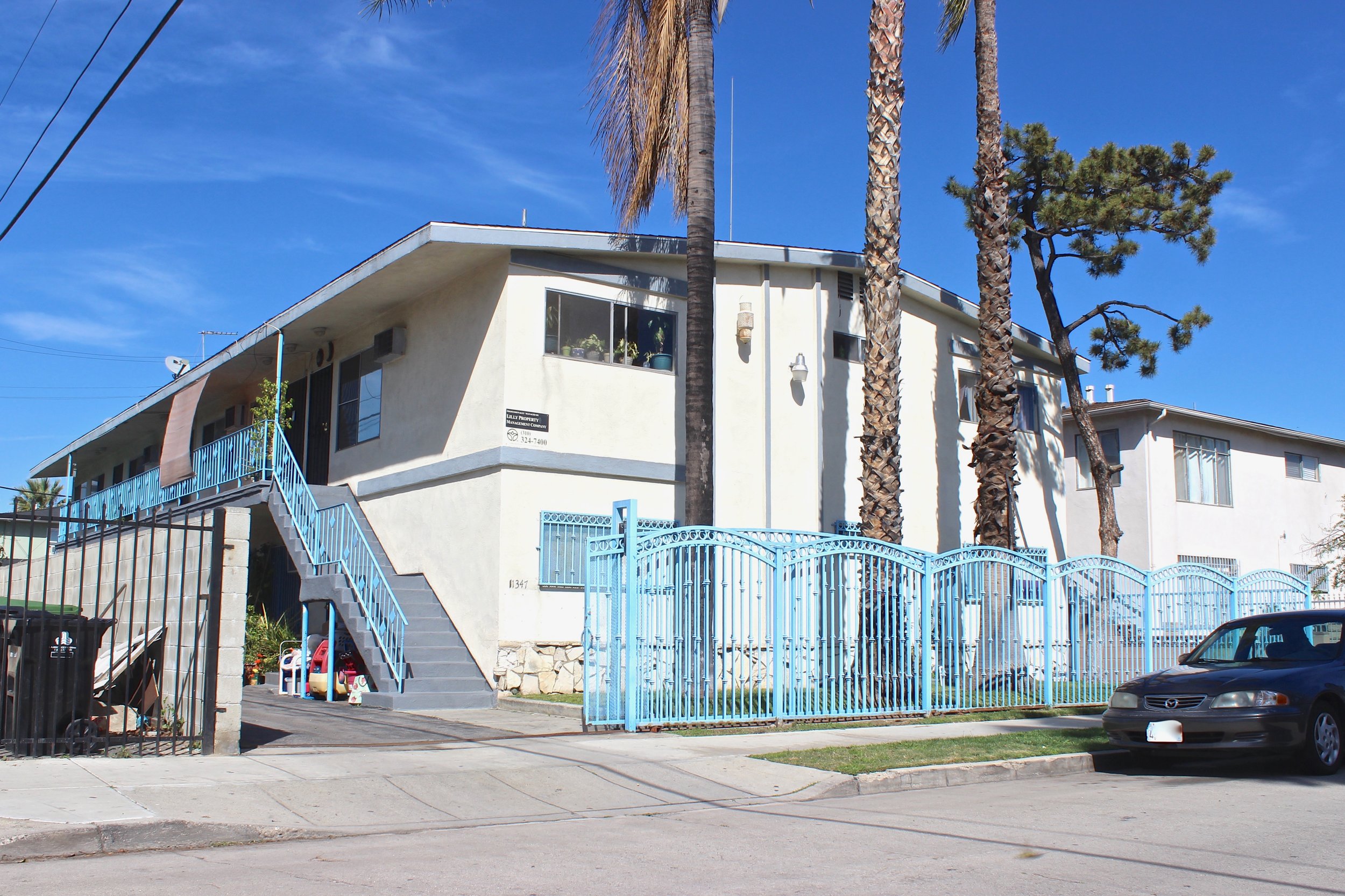 Two story apartment building with blue rod iron fence and  motorized gate leading to carports. 