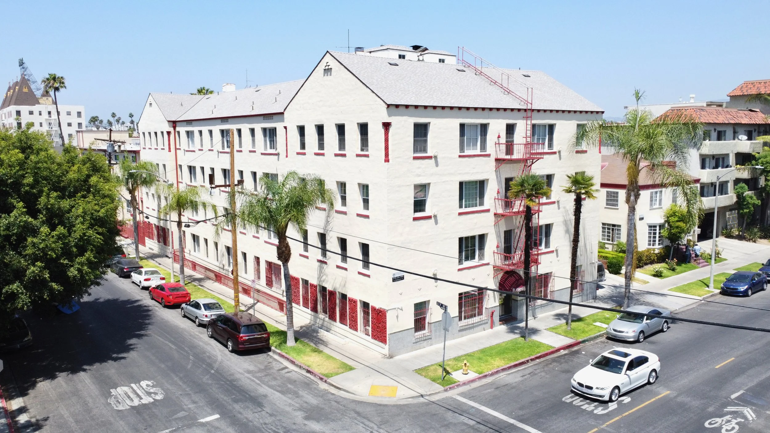 White apartment building on corner lot with red accents and  red fire escapes.