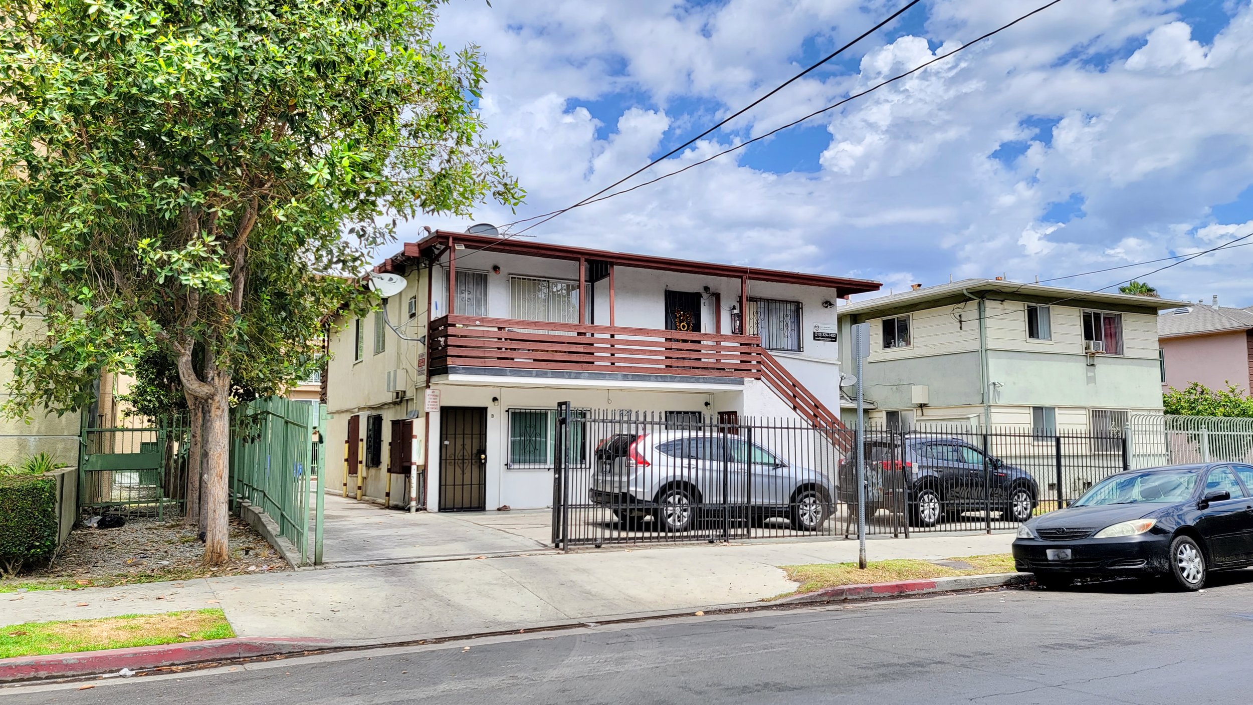 Gated two story apartment building with red exterior stairs along with motorized gate for parking.