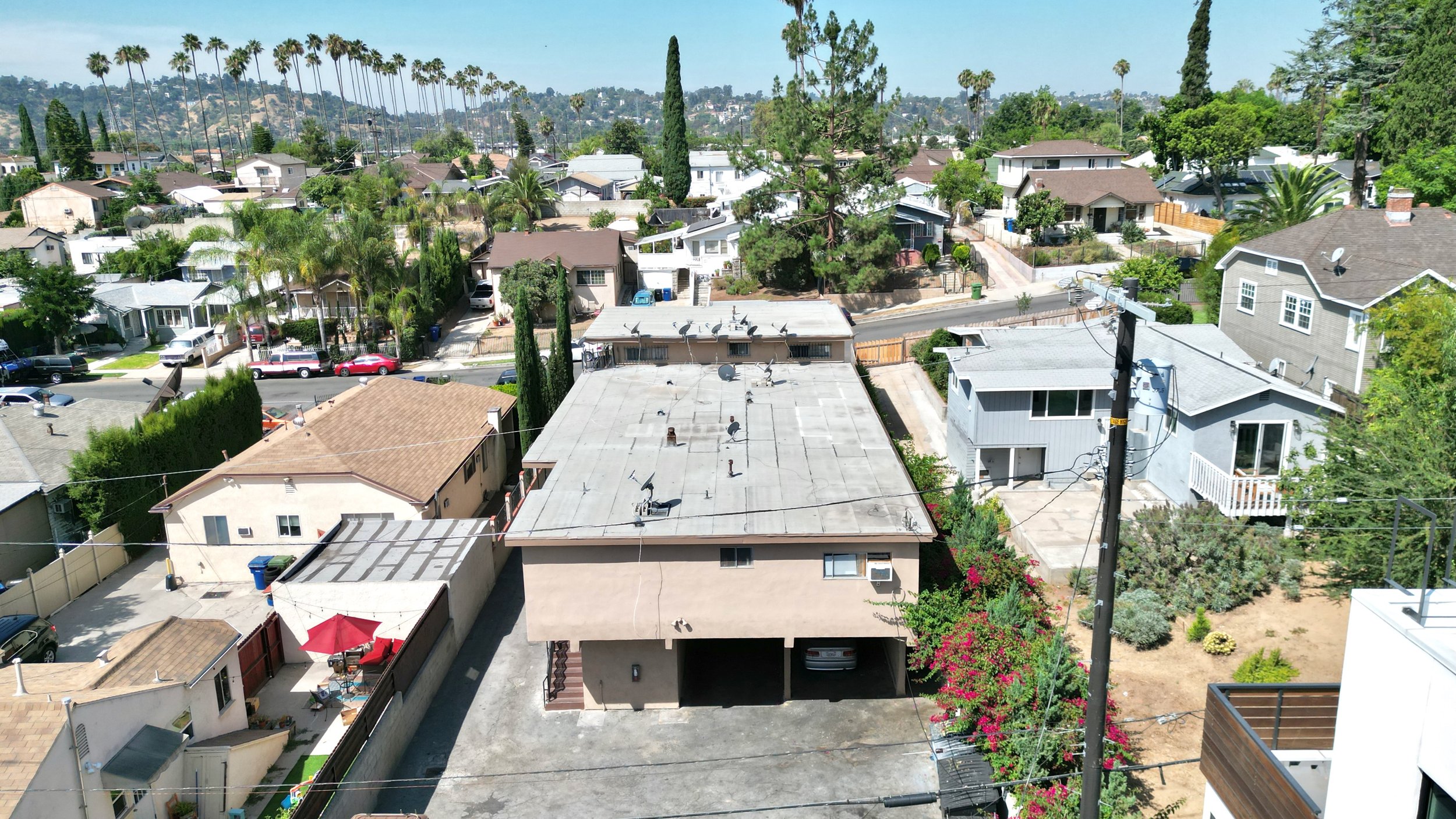 Elevated view of a neighborhood with houses, palm trees, and hills in the background.