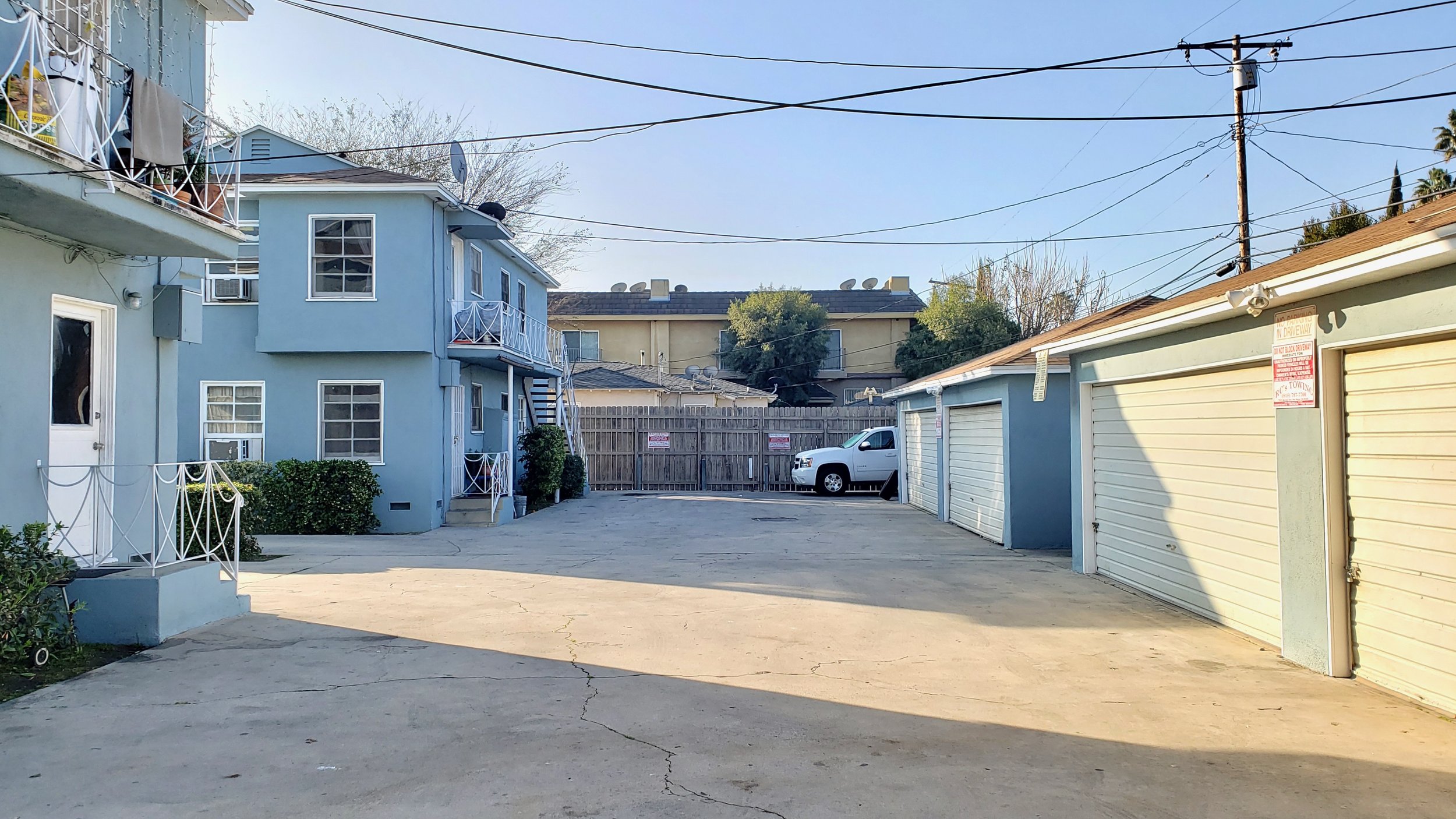 A spacious driveway with garages, a white truck, and a multi-unit light blue building under clear skies.