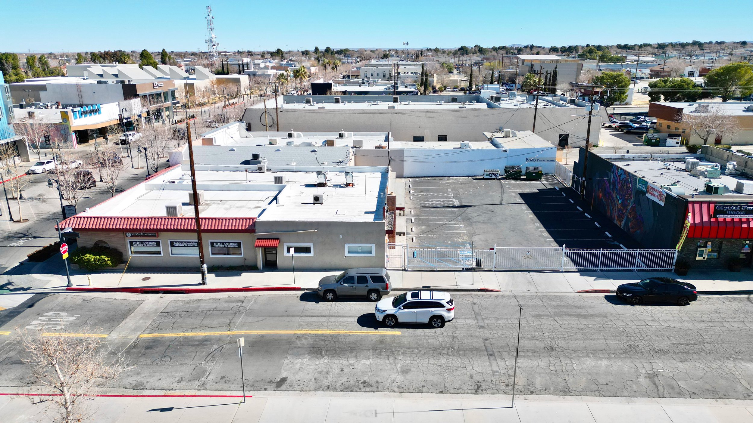 Drone shot of a street corner with red-roofed buildings, parked cars, and mural art on a clear day.