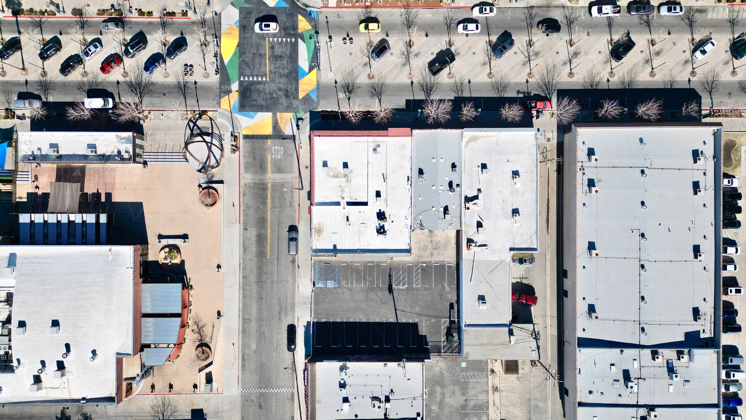 Overhead shot of urban intersection, artistic crosswalk, parked cars, and building rooftops.