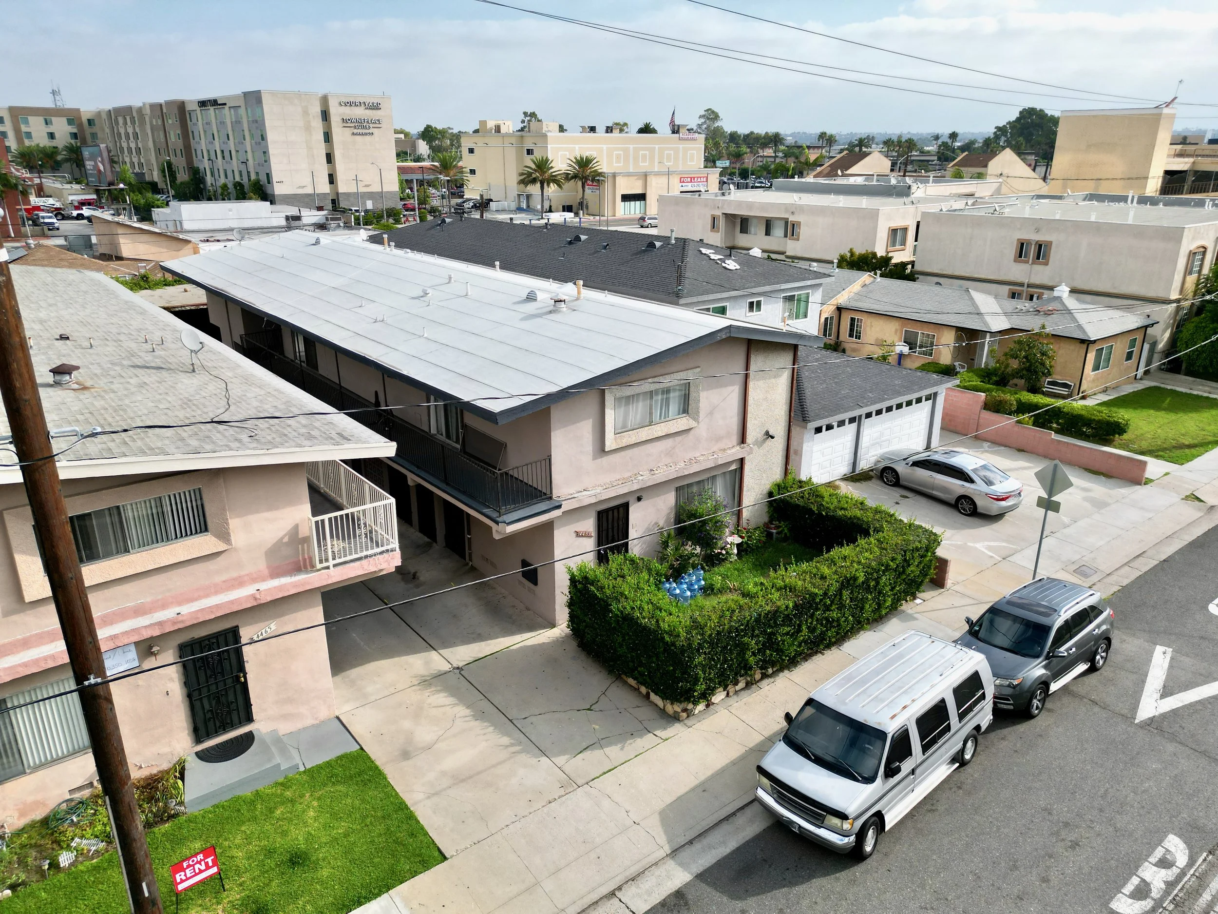 Overcast view of street with apartments, vehicles, and palms.
