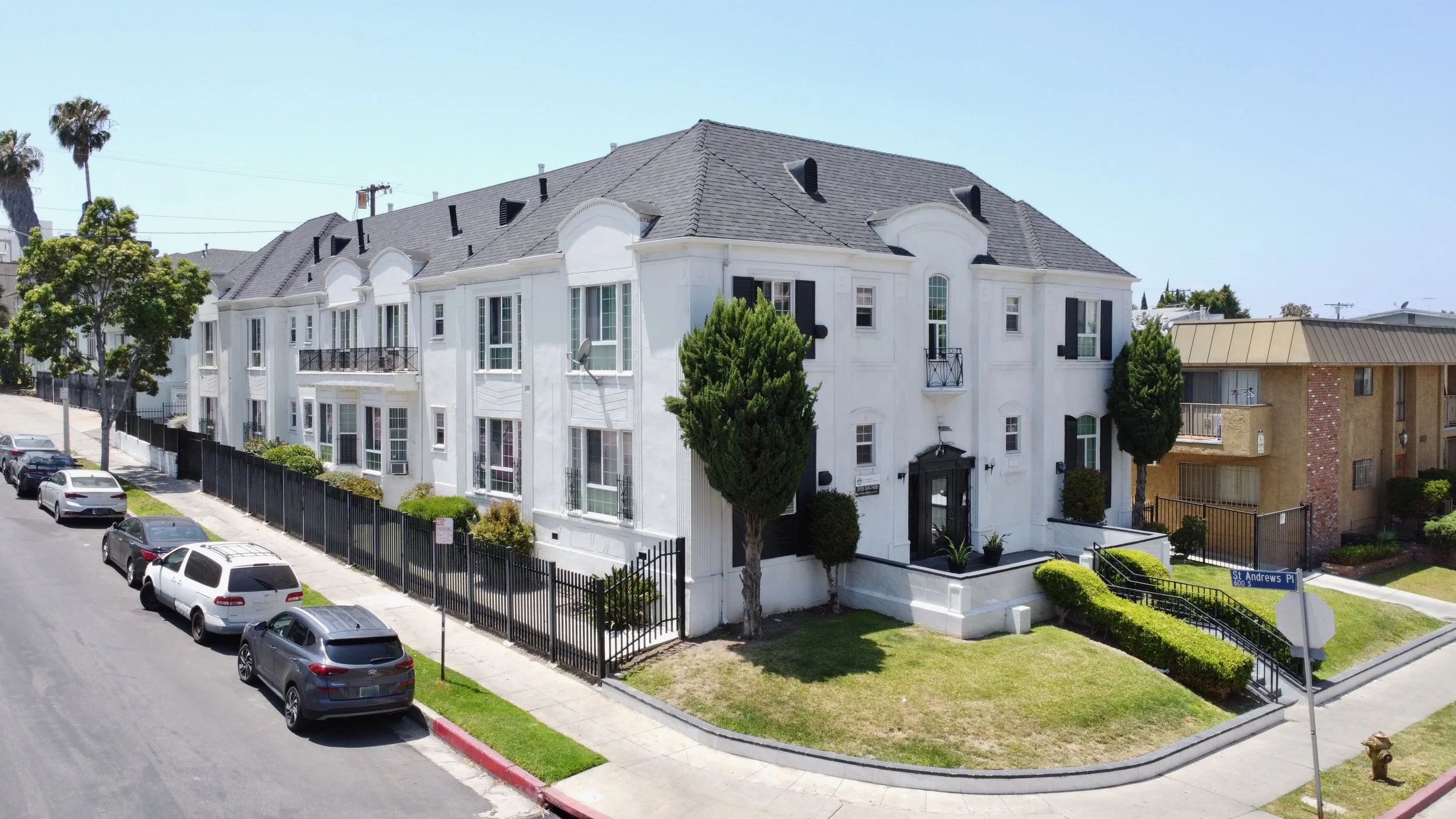 Two story white apartment complex with rod iron fence with cars curbside parked