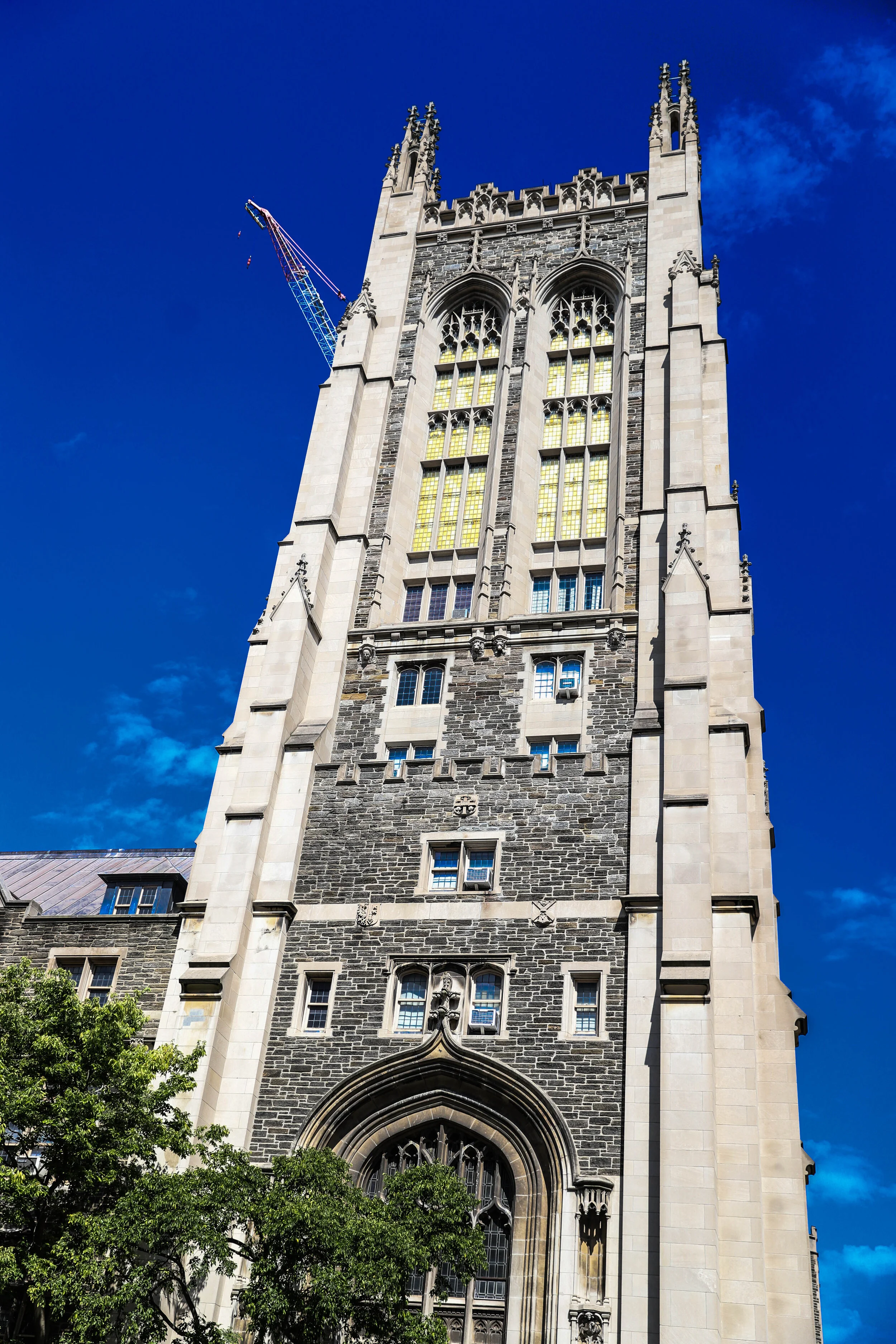 A tall, Gothic-style stone church or cathedral with stained glass windows and decorative spires, under a bright blue sky, with a construction crane visible behind the building.