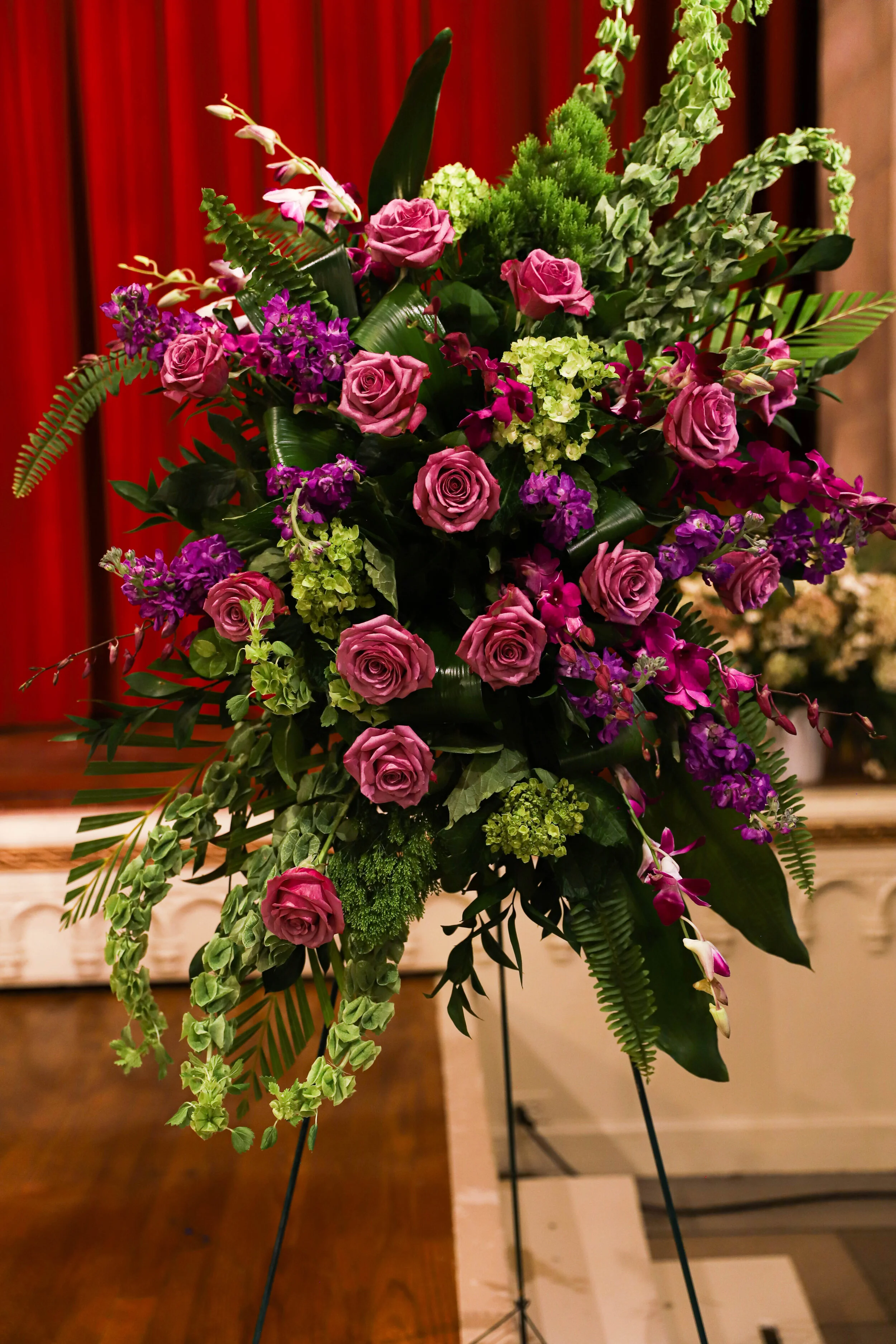 A colorful flower arrangement on display with various pink, purple, green, and white flowers, and green foliage, set against a wooden background.
