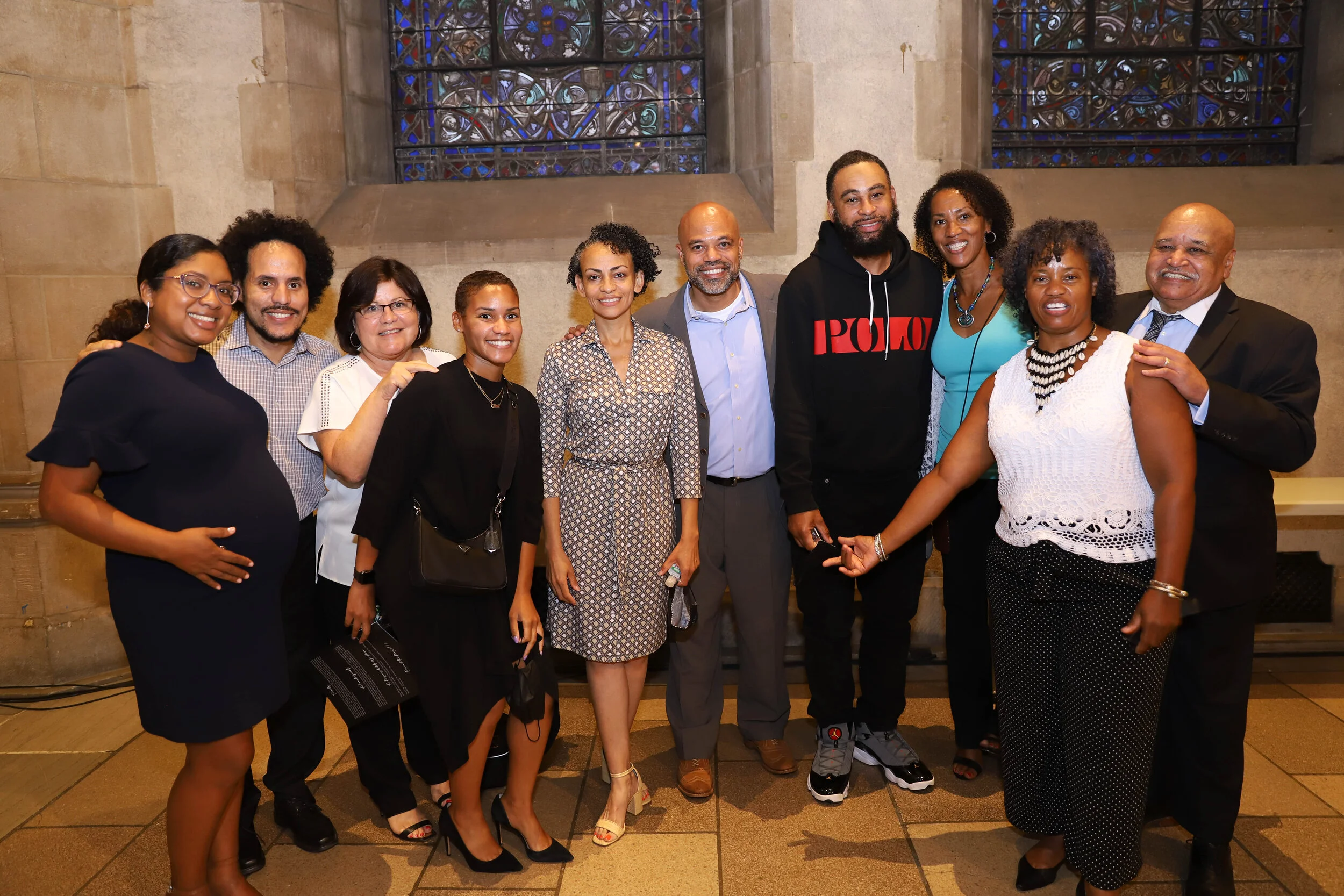 A group of eleven diverse people standing together inside a church with stained glass windows, smiling for the photo.