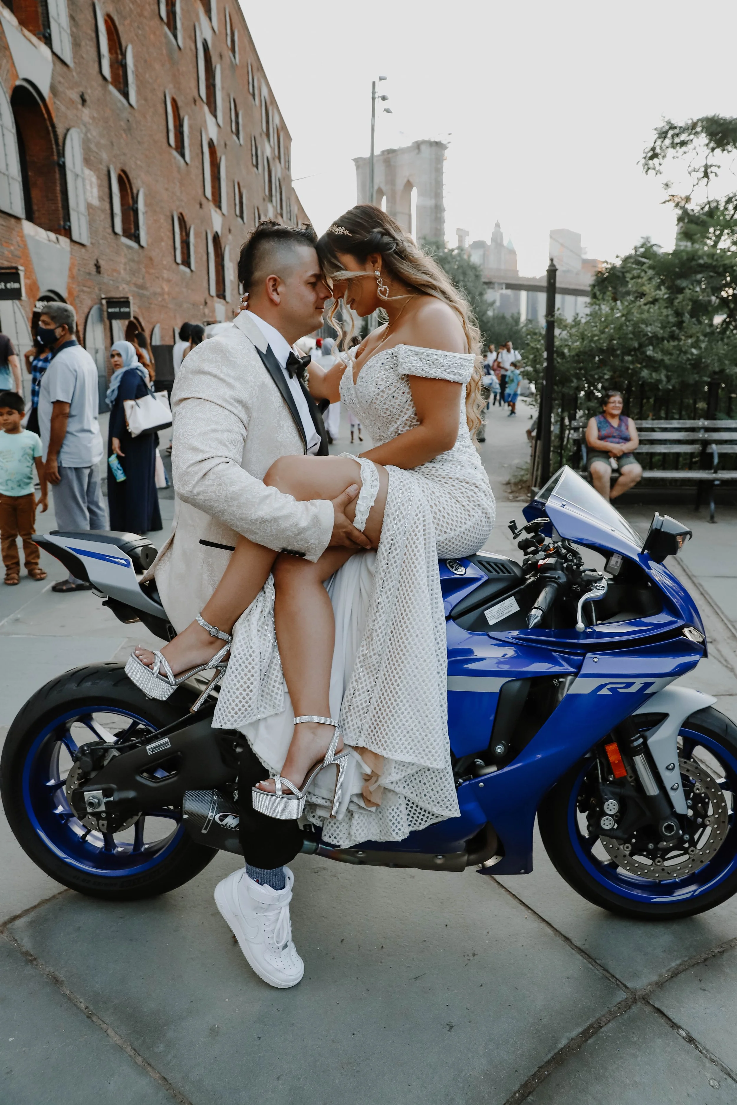 Newlywed couple embracing beside a blue motorcycle during their wedding day.