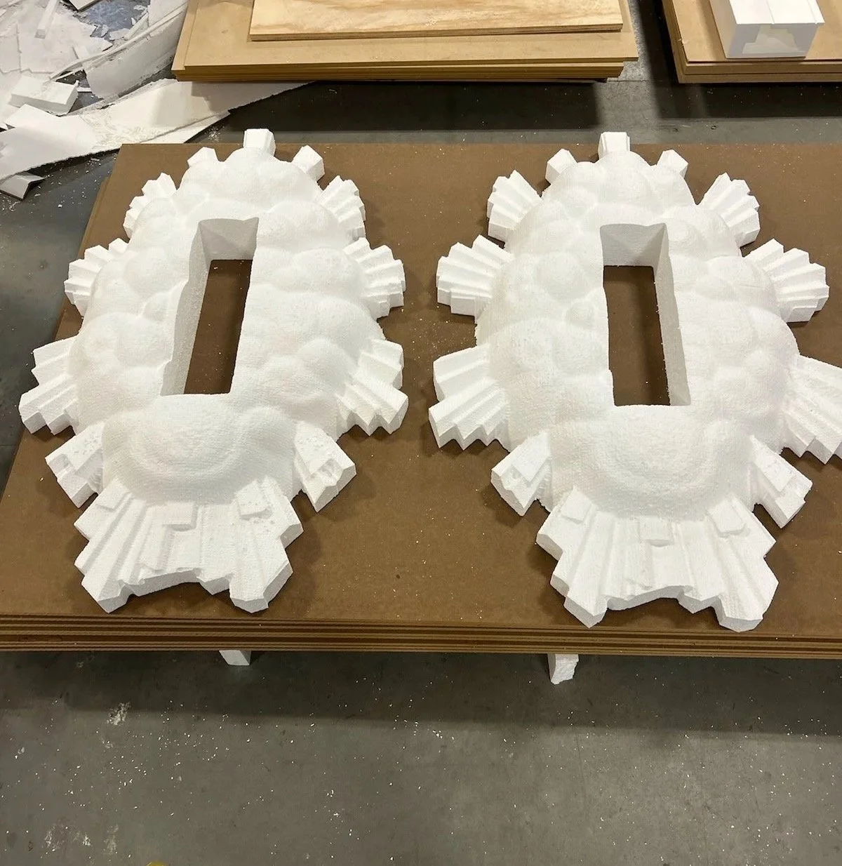Two large white foam gear-shaped pieces with rectangular cutouts in the center, placed on a worktable in a workshop.