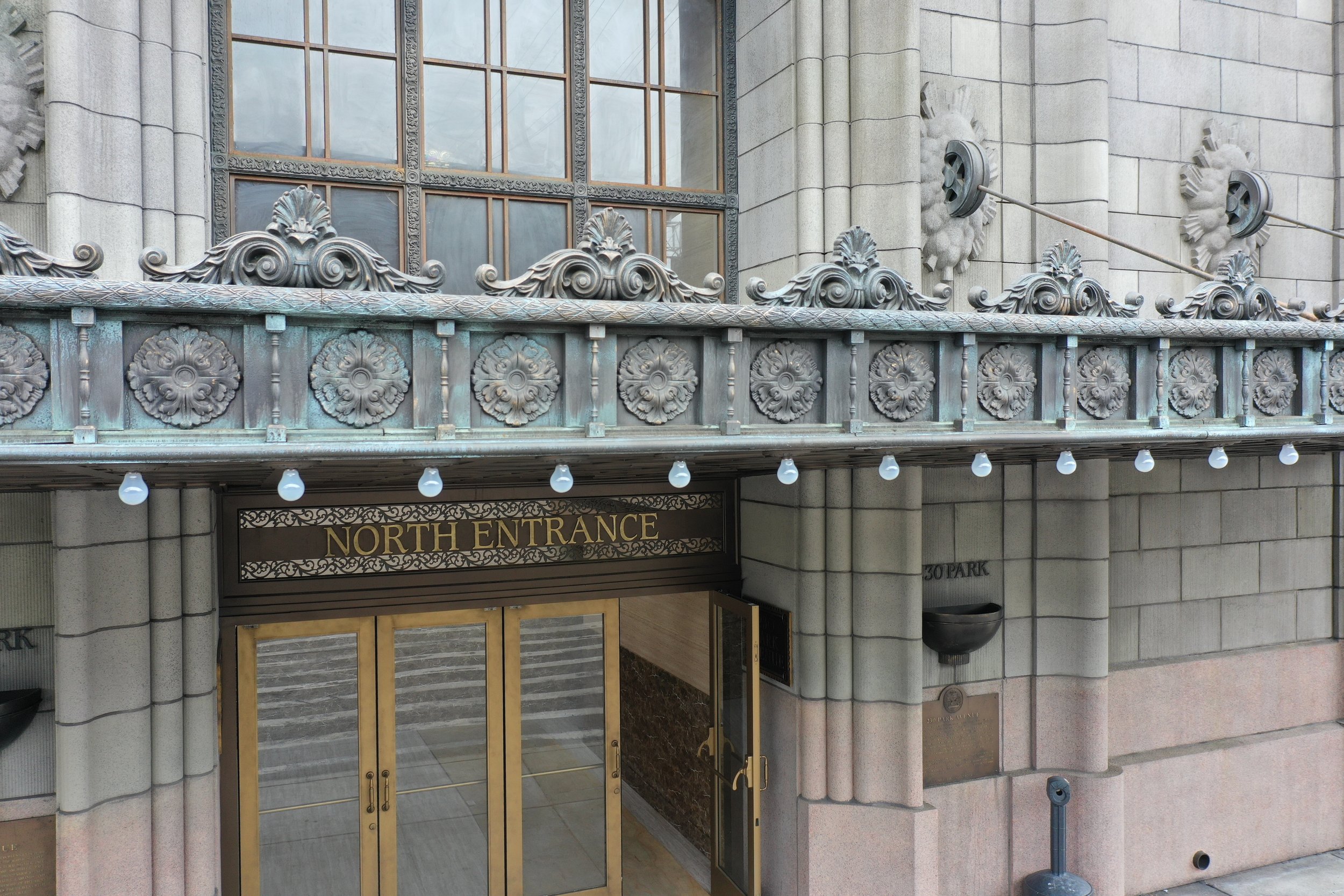 Entrance to a building with decorative metalwork, a sign that reads 'North Entrance', and stairs leading inside.