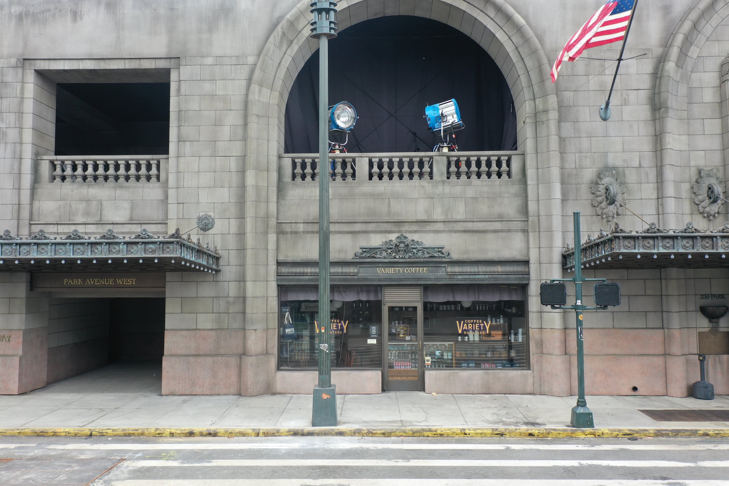 Empty building with signs that say "Park Avenue West" and "Variety Coffee", two large spotlights on the balcony, a streetlamp in front, and American flag hanging on the right side.