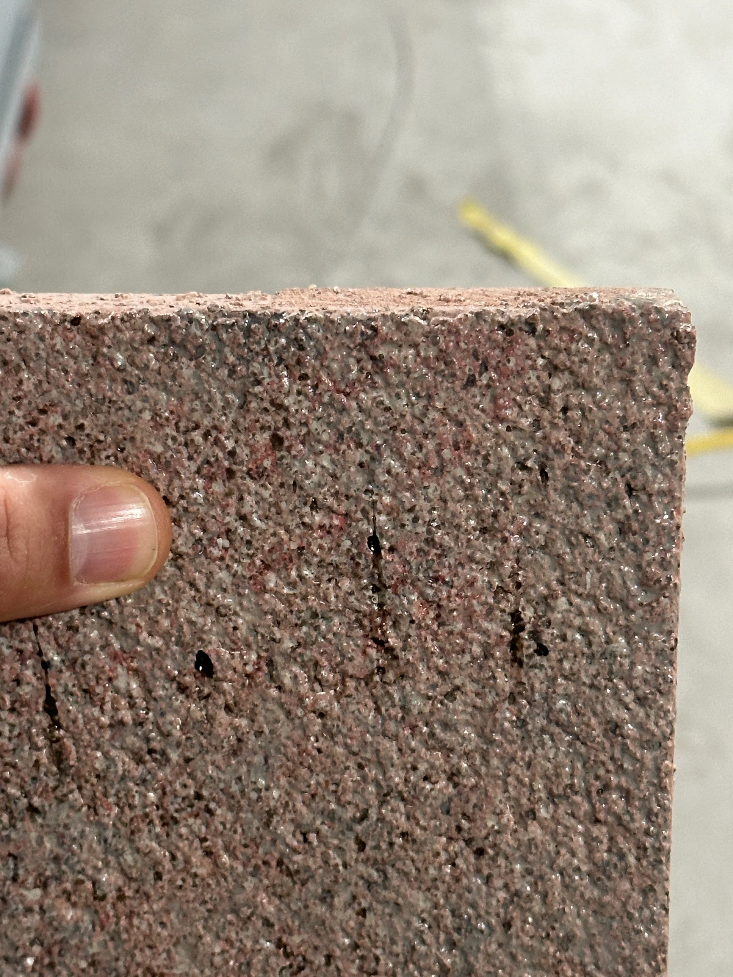 Close-up of a textured reddish-brown concrete or cinder block with a person's thumb holding the left side.