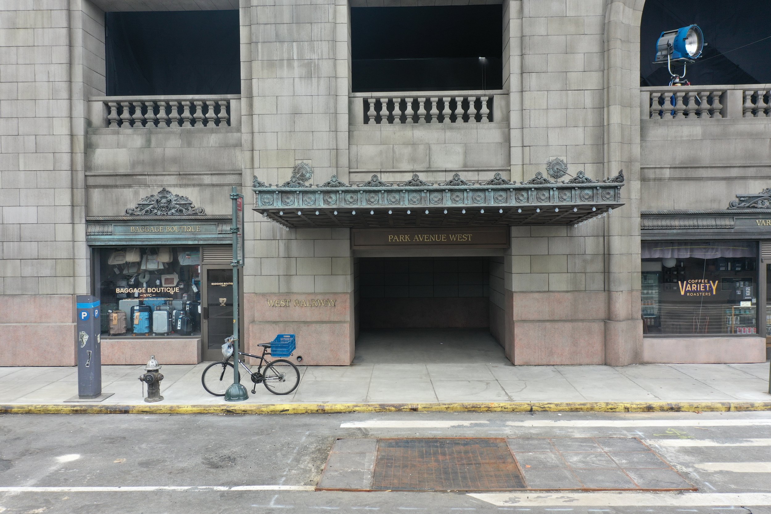 Street view of a building with shops, a bicycle secured to a pole, a parking meter, a fire hydrant, and a yellow-painted curb. The building has signs indicating "Baggage Boutique" and "Coffee Variety Roasters," with an entrance labeled "Park Avenue W